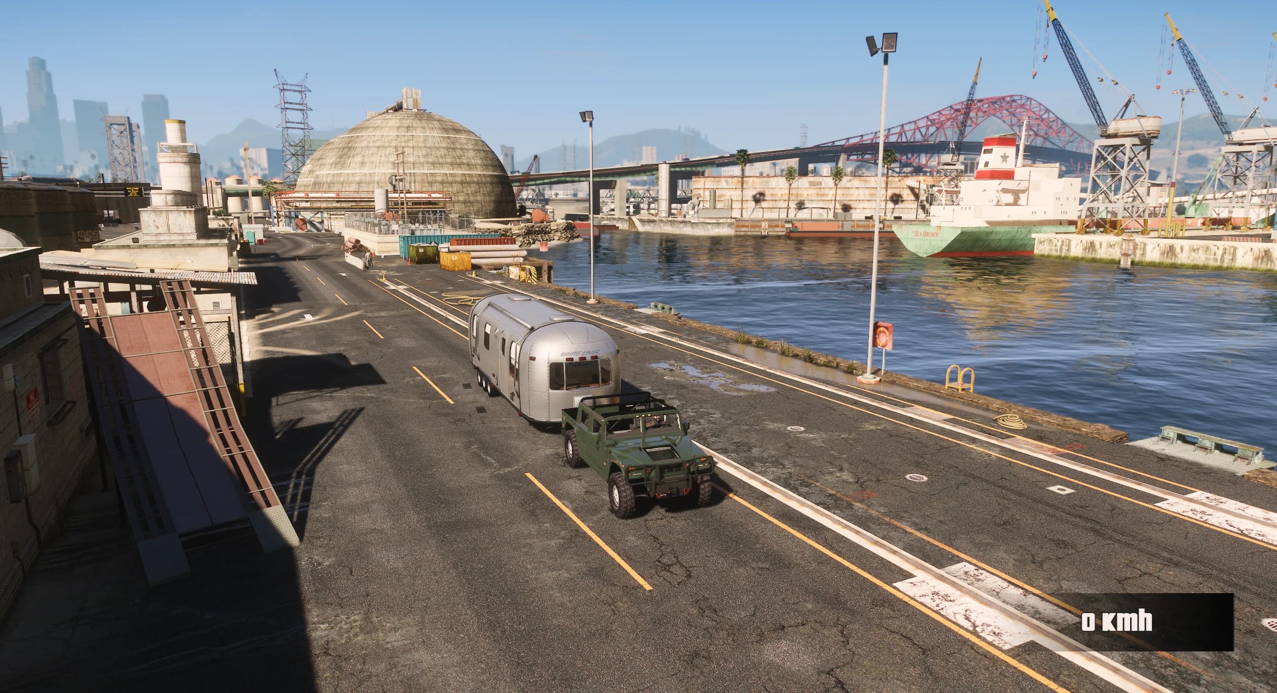 Elevated dockside view of the green H1 Alpha Open Top beside a silver caravan, with cranes, a moored cargo ship and the port bridge in the background