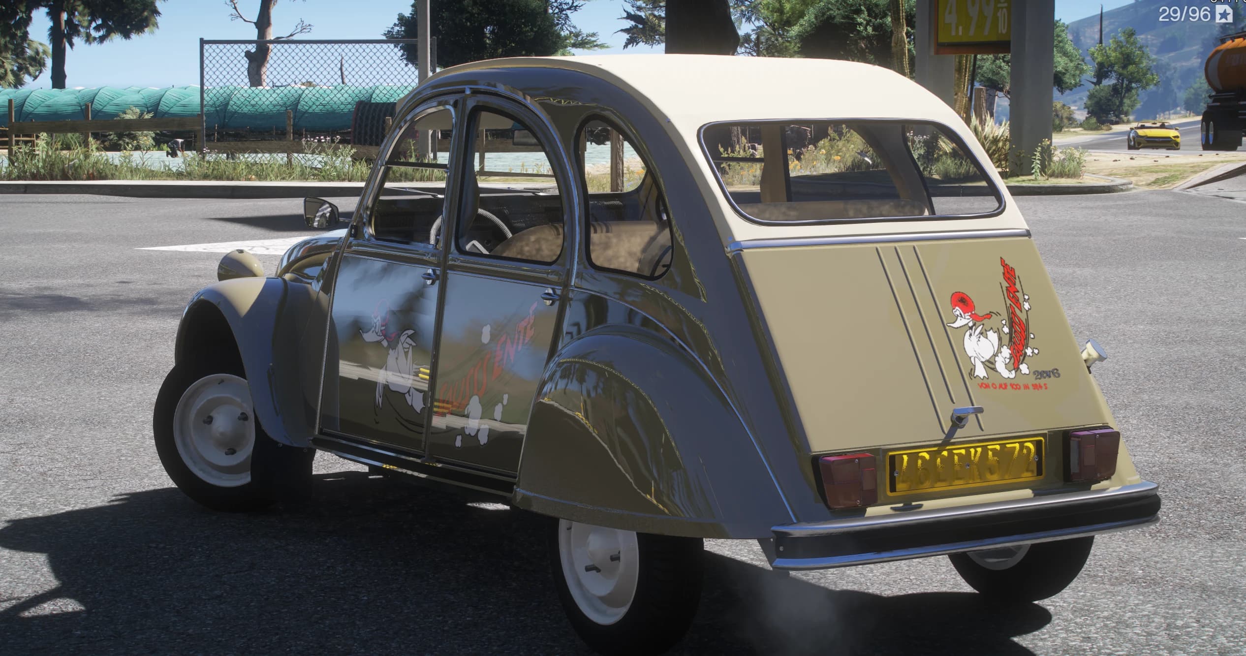 Rear view with the duck decal and 2CV6 lettering on the boot lid and a yellow rear plate, at a petrol station