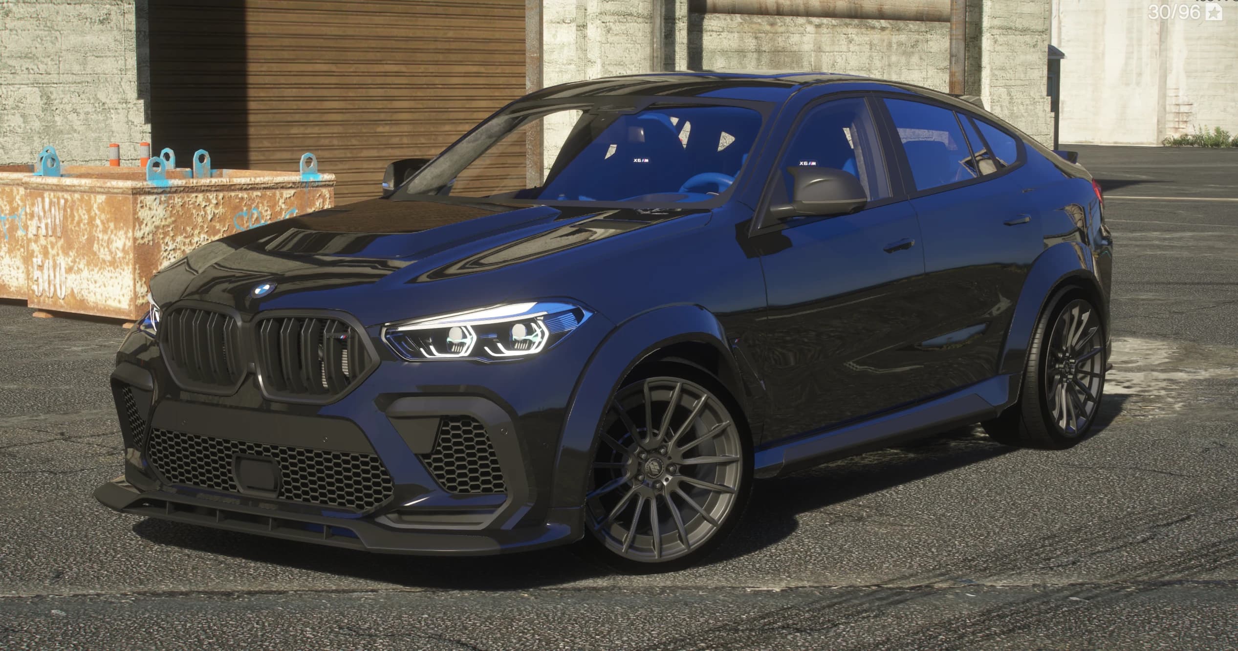 Front three-quarter of the dark blue 2023 BMW X6M with the Prior Design widebody kit, showing the blacked-out kidney grille with a red M accent, the carbon front splitter, flared arches and the blue M interior with X6 M seats