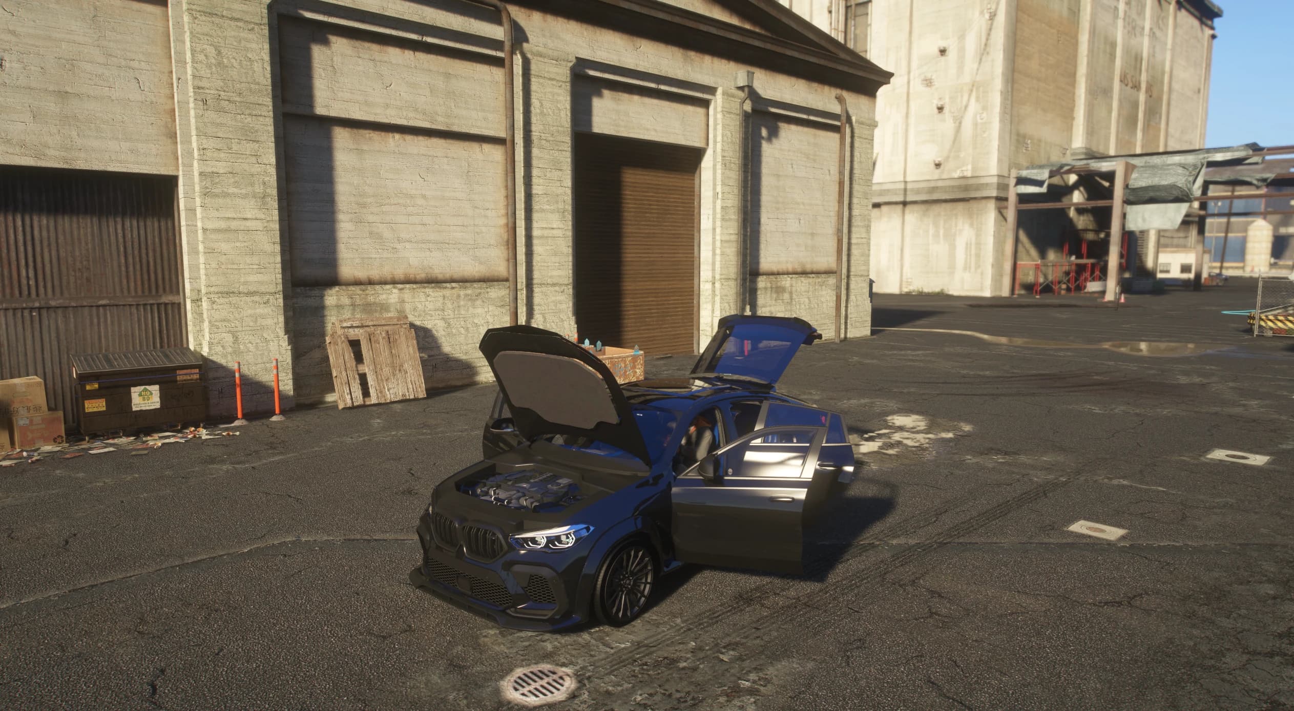 The dark blue X6M with the hood and doors open, revealing the twin-turbo V8 engine bay and the blue interior, parked in front of a concrete dockside silo