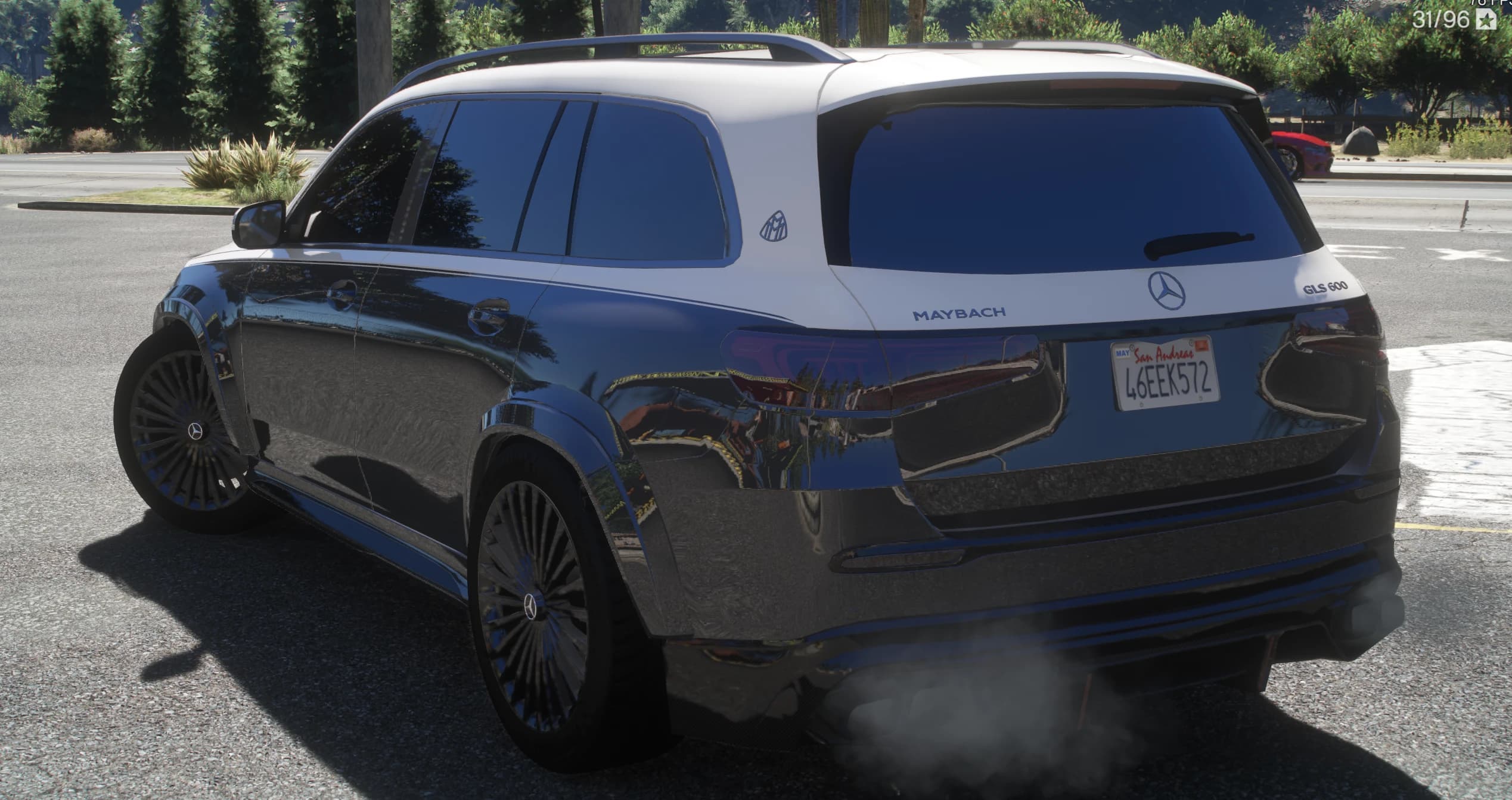 Rear three quarter view by a tree lined road showing the MAYBACH and GLS 600 lettering on the tailgate, the Maybach emblem on the pillar and exhaust smoke