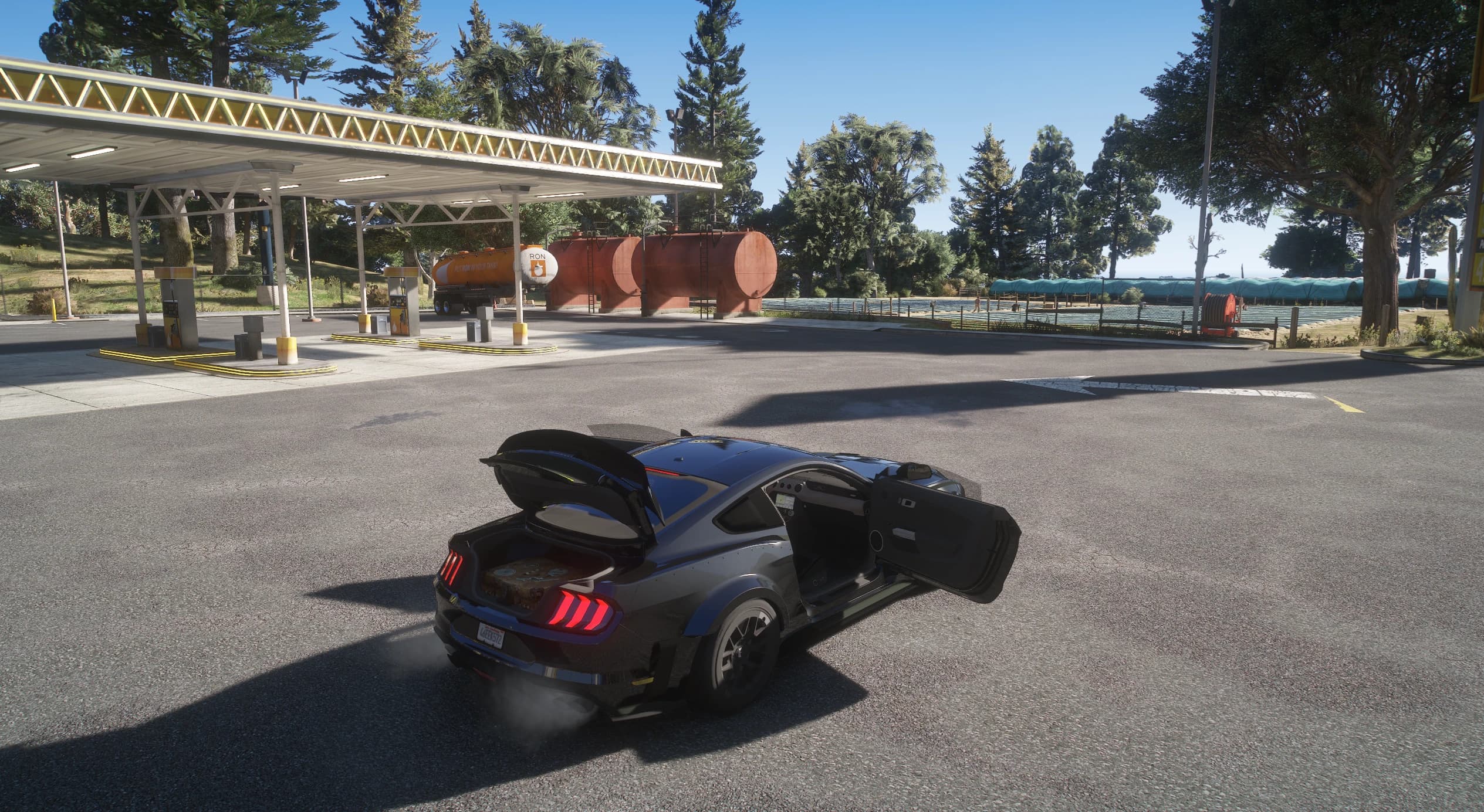 High angle of the Mustang at a RON petrol station with the trunk lid and the driver's door open, the wing lifting with the lid and the rear lights on