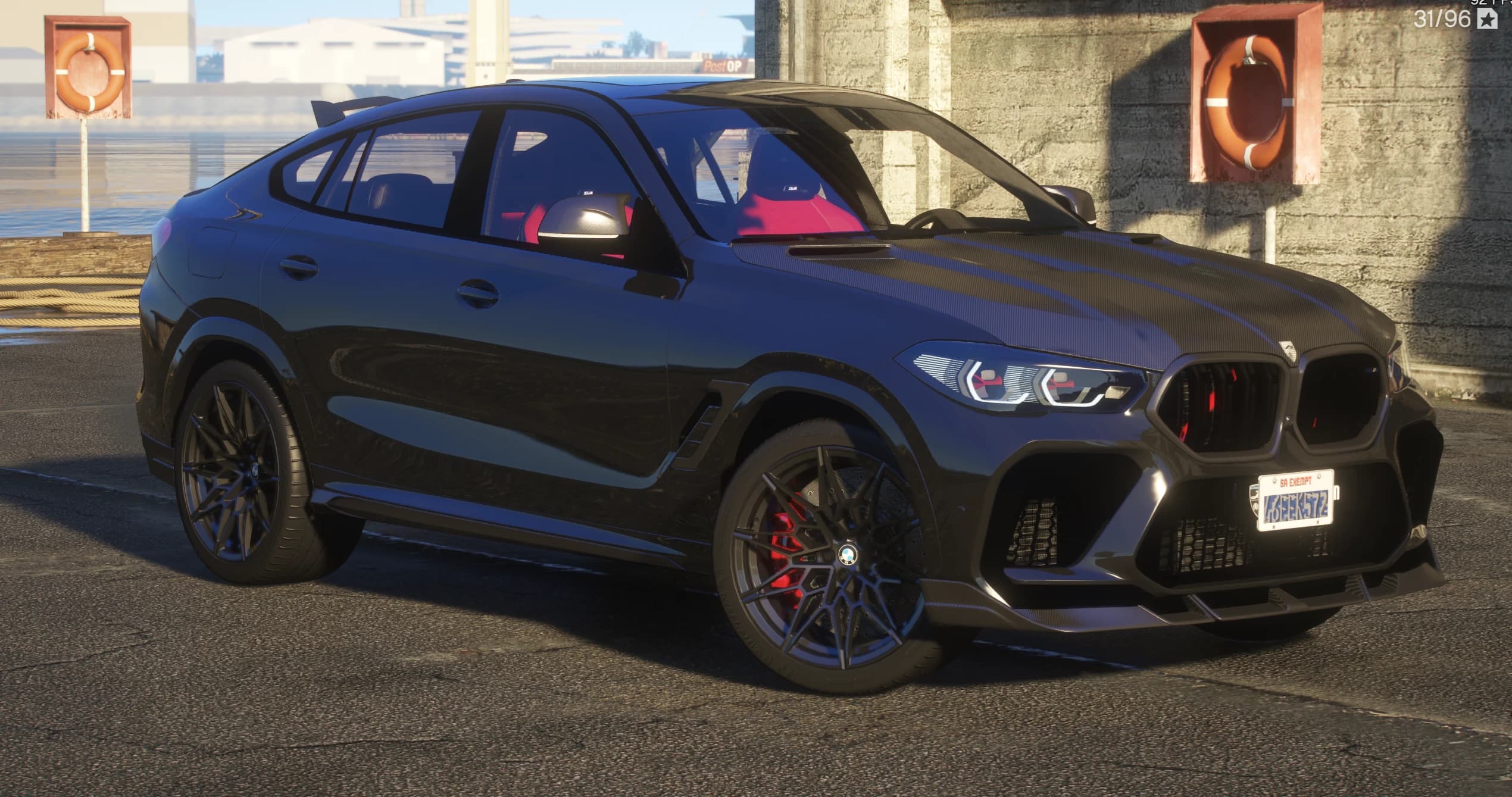 Front three quarter view of the black BMW X6M with the carbon hood, red trimmed kidney grilles, carbon front splitter and red sport seats visible through the glass, parked at the docks