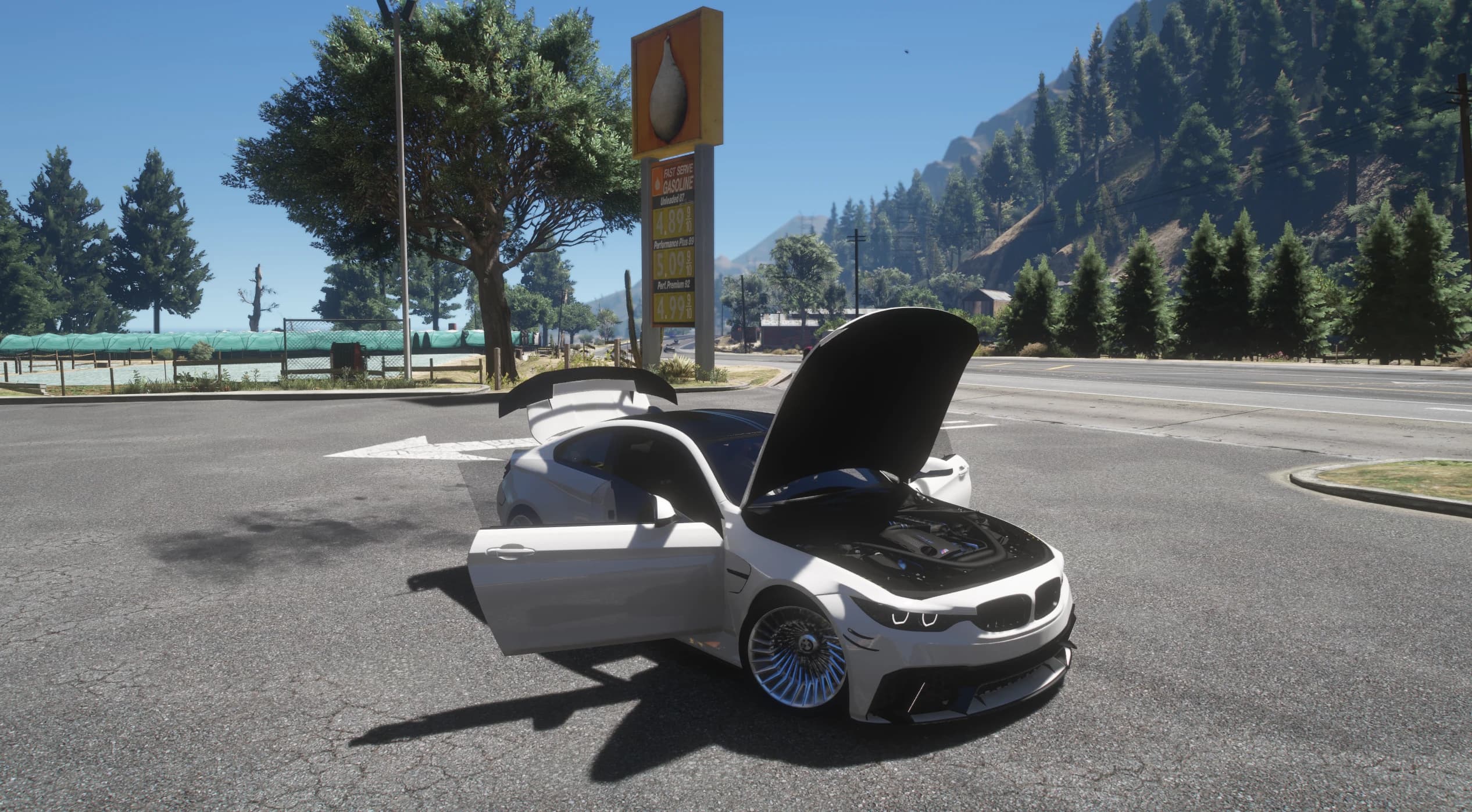 Wide shot at a mountain gas station with the M4's hood, doors and trunk open over the engine bay