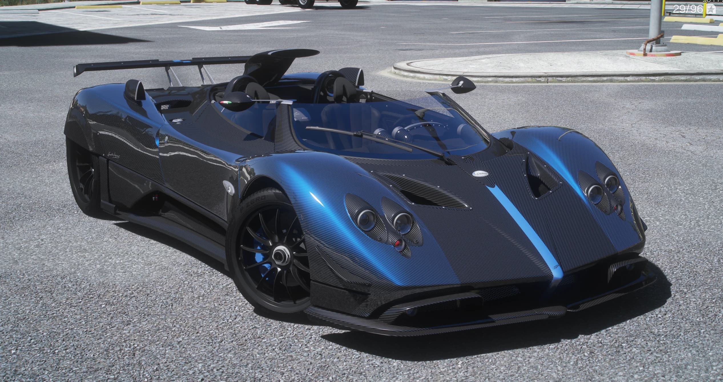 Carbon-fibre Pagani Zonda HP Barchetta roadster with a blue centre stripe, front three-quarter view, open-top with quad round headlights, a tall rear wing and Pirelli tyres