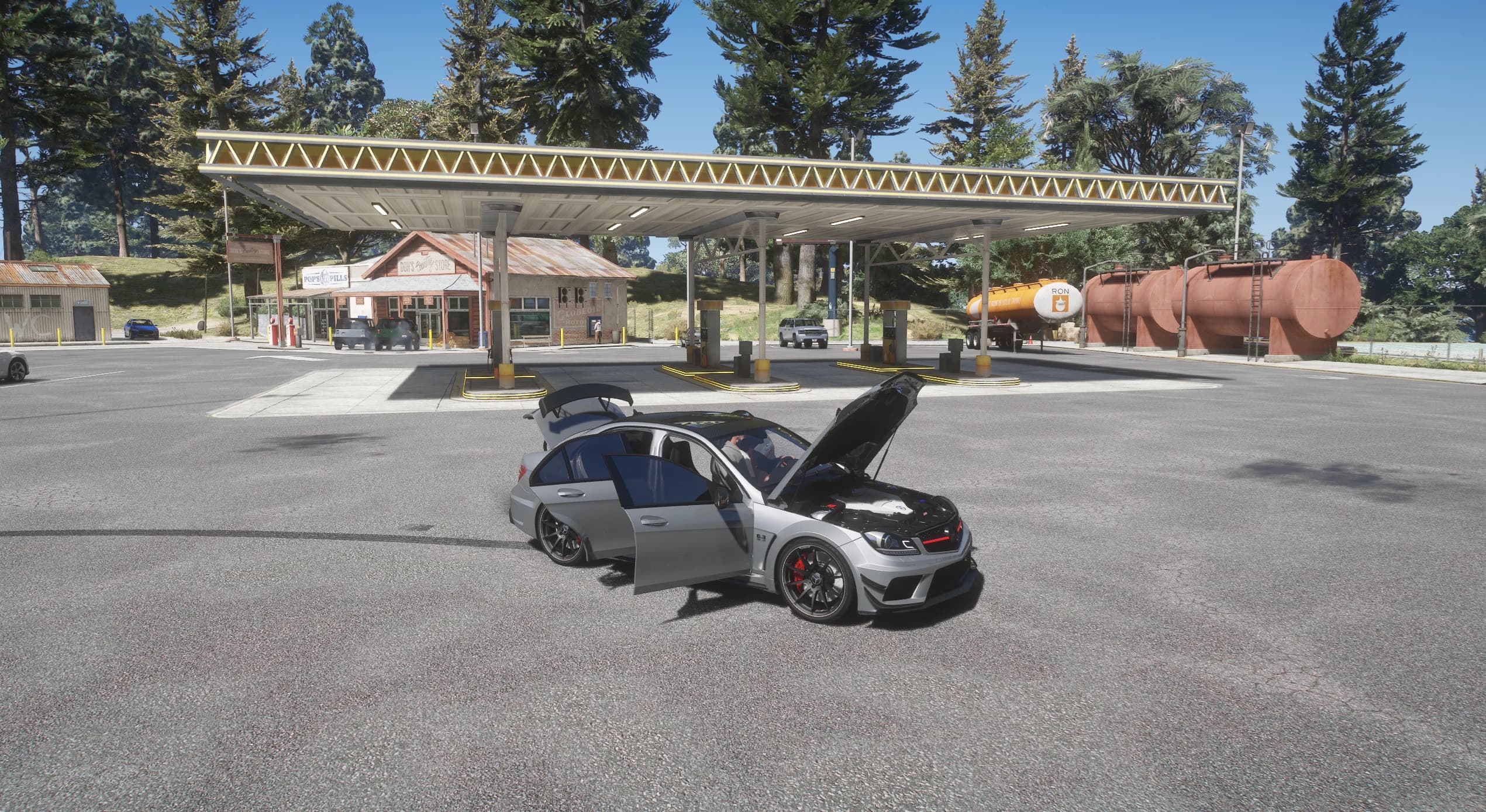Wide shot of the C63 on the forecourt of a country petrol station with the hood, the two left doors and the boot open, showing the modelled engine bay, with fuel tanks and a store behind