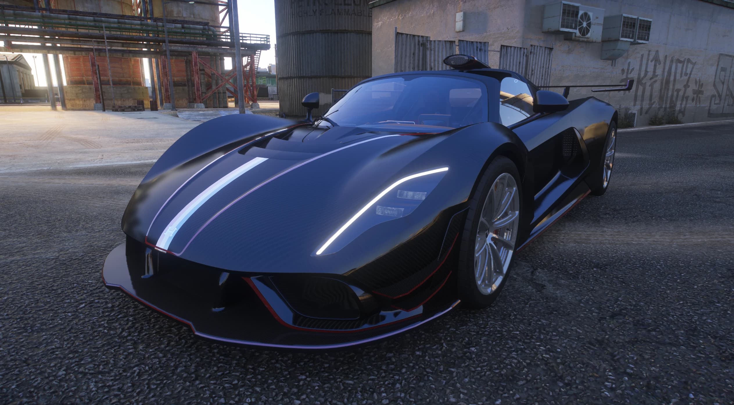 The Venom F5 Roadster in a black carbon finish with a white stripe, front three-quarter view beside an industrial building