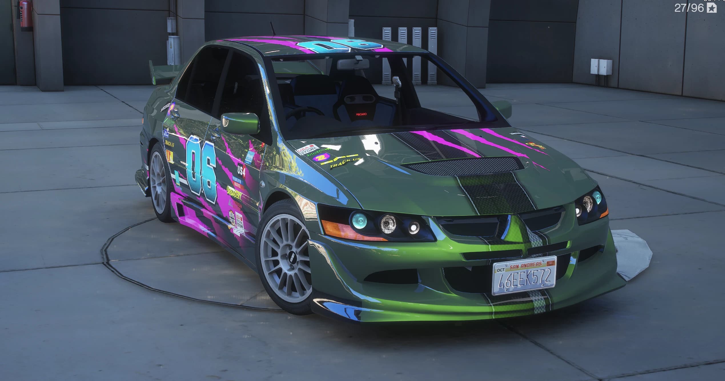 Green 2003 Lancer Evolution VIII in front three-quarter view on a concrete turntable, wearing a pink and cyan number 06 racing wrap, white multi-spoke wheels and a San Andreas plate