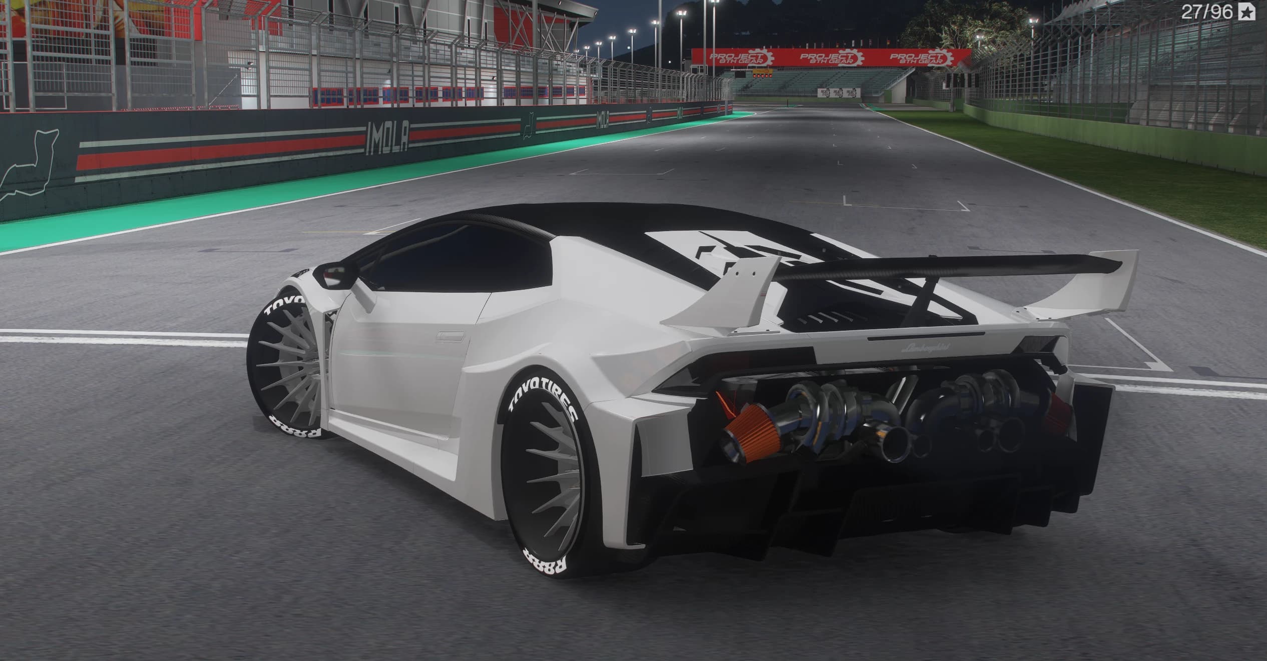 Rear three-quarter of the white Huracan at night on the pit straight, with the exposed V10 and its intakes visible behind the cabin, the big rear wing and the wide Toyo-lettered tyres