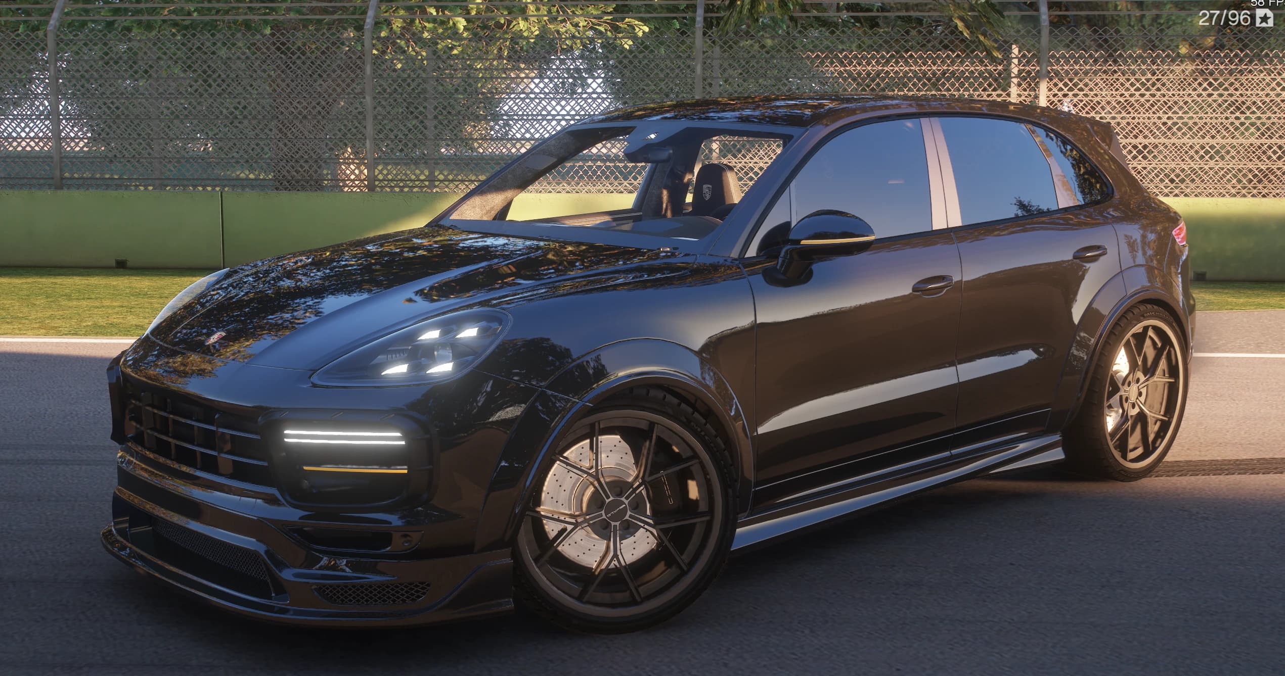 Gloss black Porsche Cayenne with the Wald Black Bison kit, front three-quarter view on a circuit access road, showing the LED bar in the front apron, the widened arches and the cabin visible through the open driver's window with the Porsche crest on the headrest
