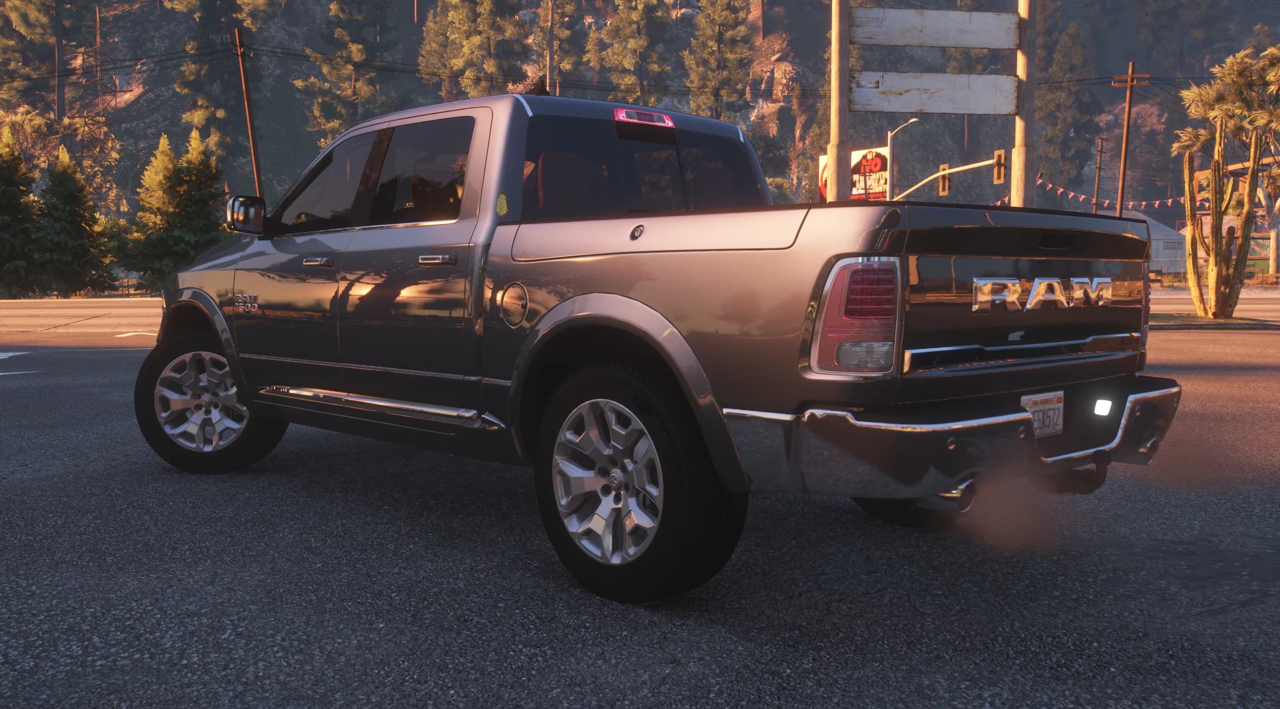 Rear three quarter view at sunset with the chrome RAM lettering across the tailgate, twin exhausts and a cactus lined mountain road behind