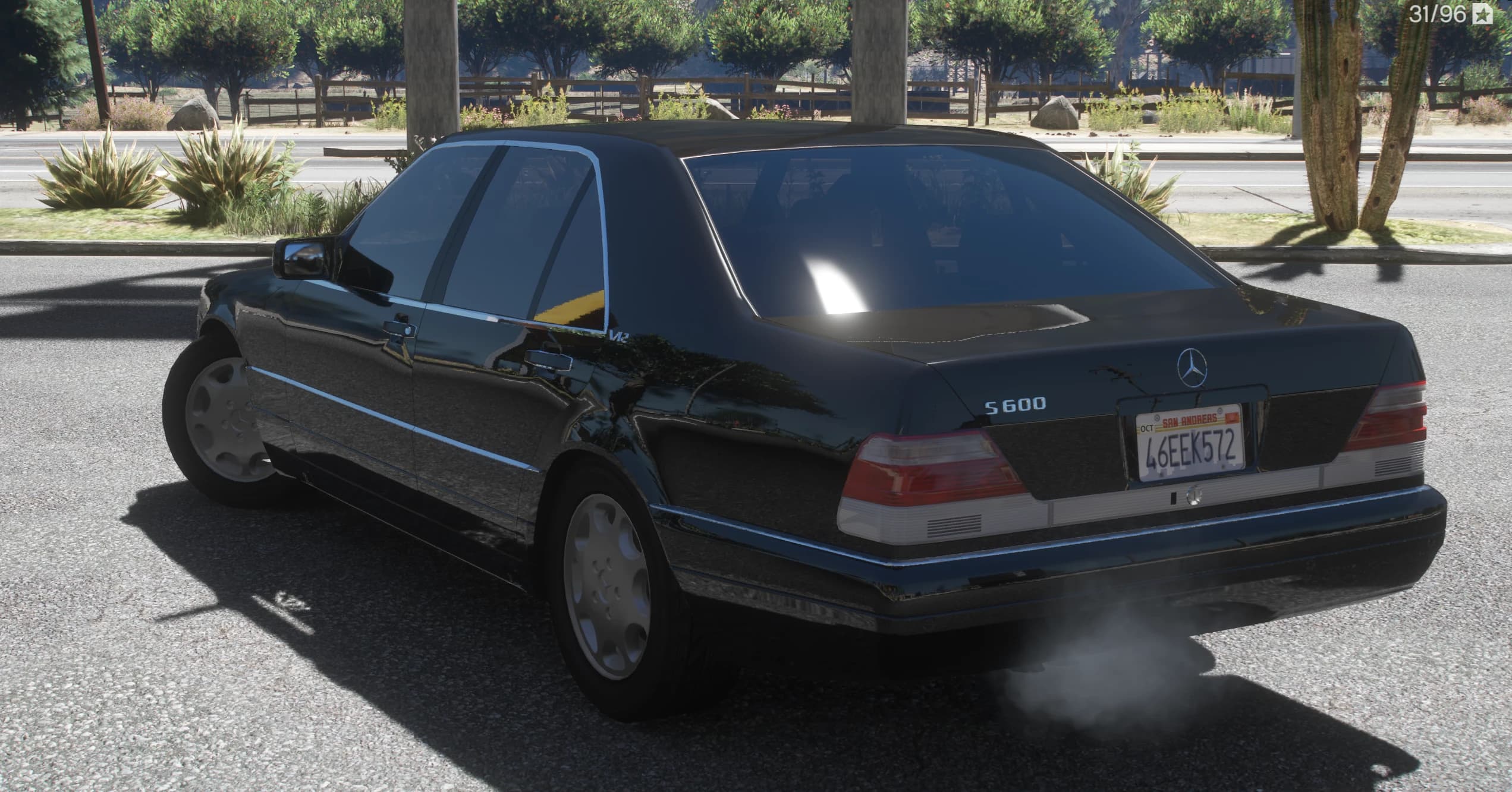 Rear three quarter with the S600 boot badge, the V12 emblem on the pillar and exhaust smoke, with a wooden country fence behind