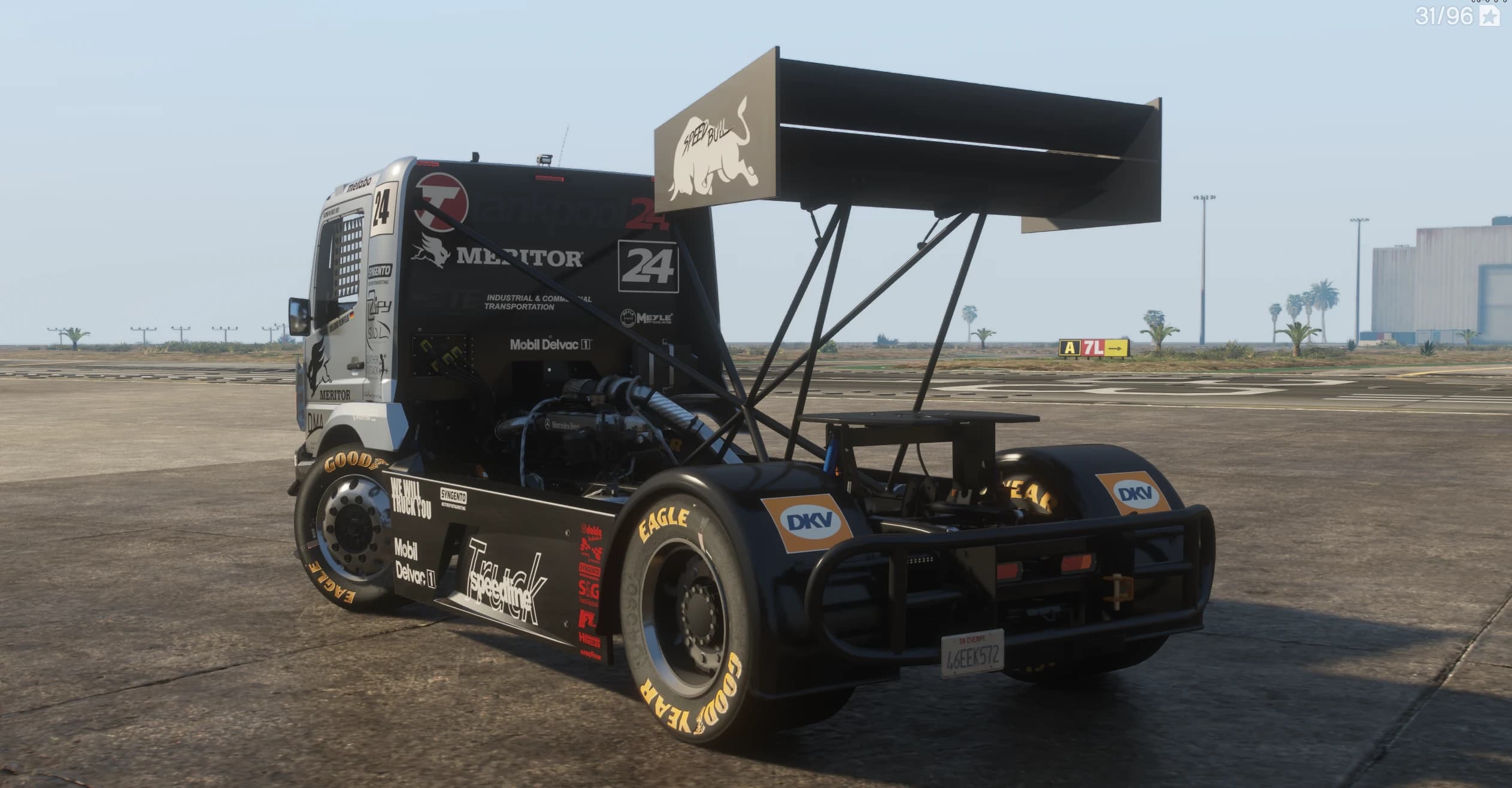 Rear three quarter view on an airfield showing the exposed engine behind the cab, the huge rear wing with a charging bull graphic and gold lettered Goodyear tyres