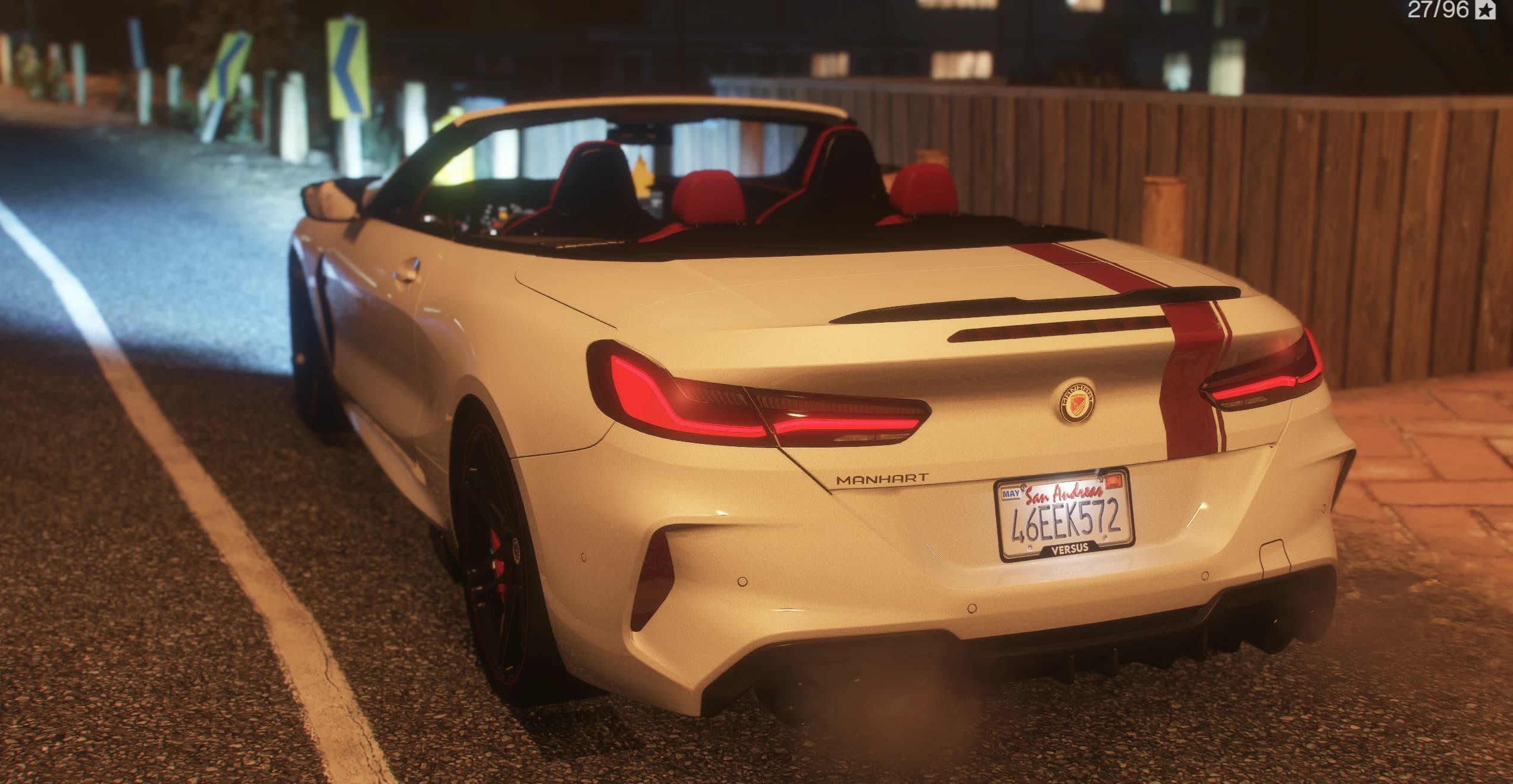 Rear three-quarter of the MH8 800 at night: the red stripe runs over the trunk lid, the red leather seats are exposed with the roof folded away, MANHART lettering sits on the tailgate and the plate frame reads VERSUS