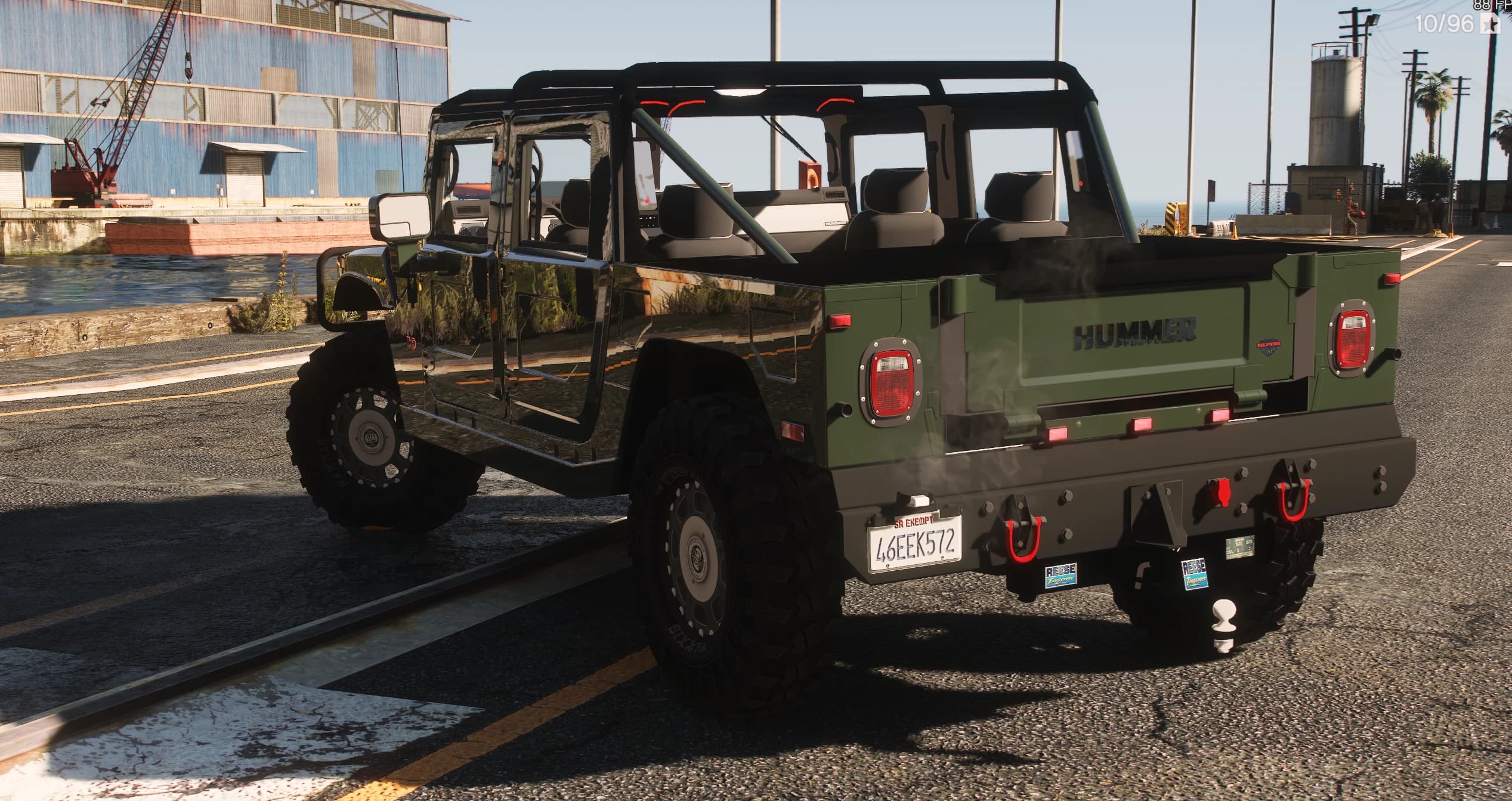 Rear three-quarter of the green H1 with the HUMMER lettering on the tailgate, red tail lights, tow hooks and a hitch ball on the rear bumper, and the open roll-caged cabin with its seats in view