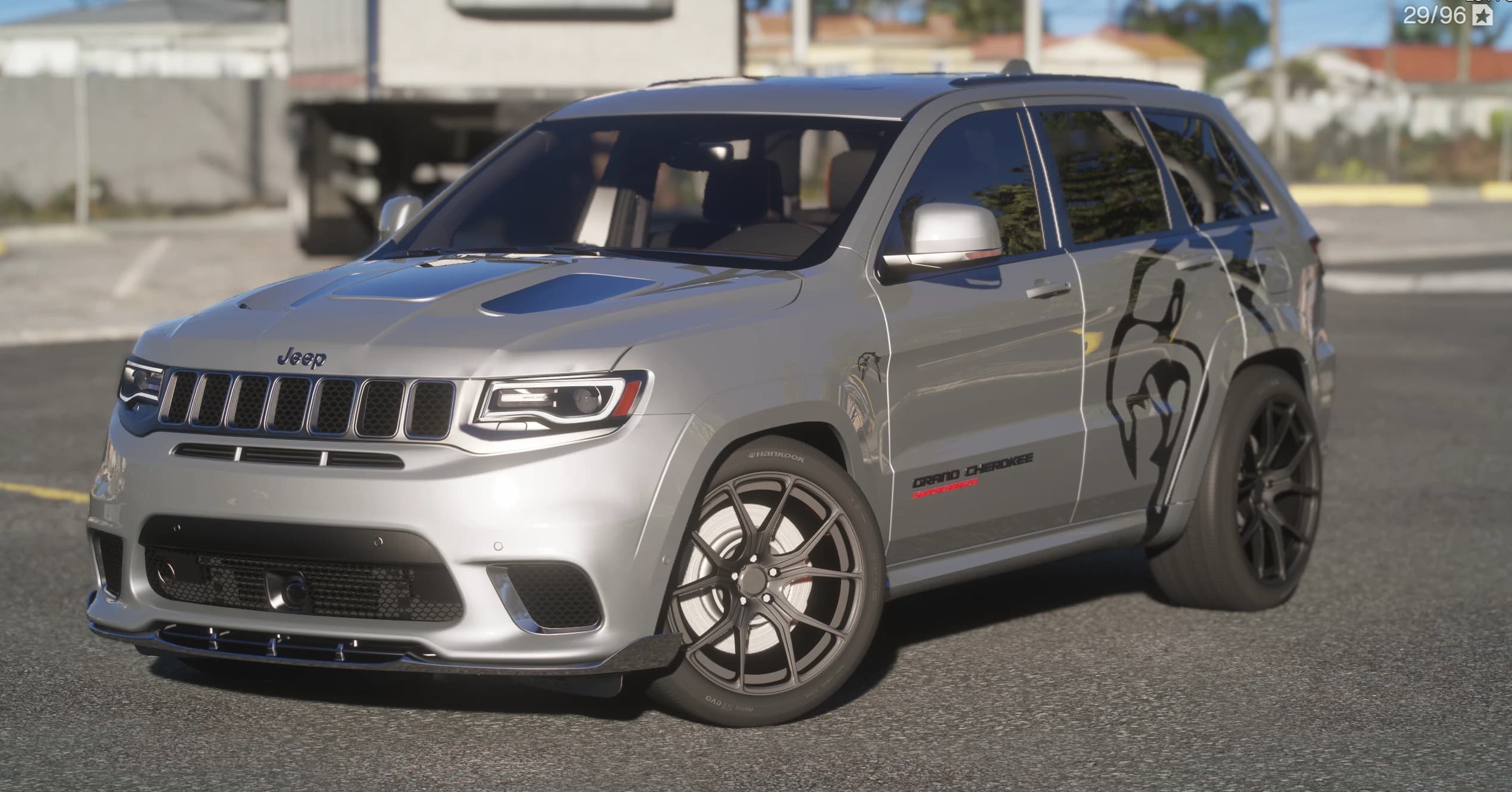 Silver Jeep Grand Cherokee Trackhawk, front three-quarter view with the hood scoop, the Grand Cherokee Supercharged badge, black wheels and a black lion graphic on the rear quarter