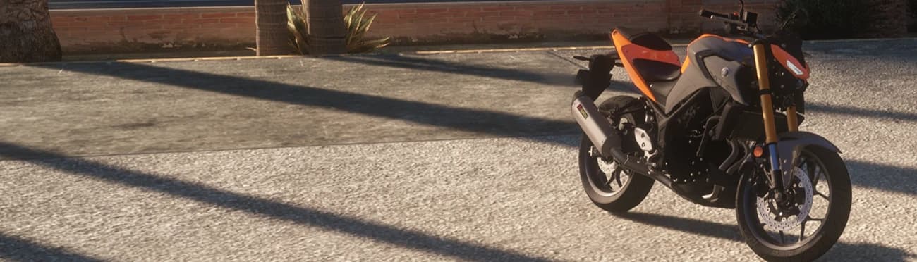 Wide shot of the orange MT-03 parked on a sunlit concrete lot with palm shadows