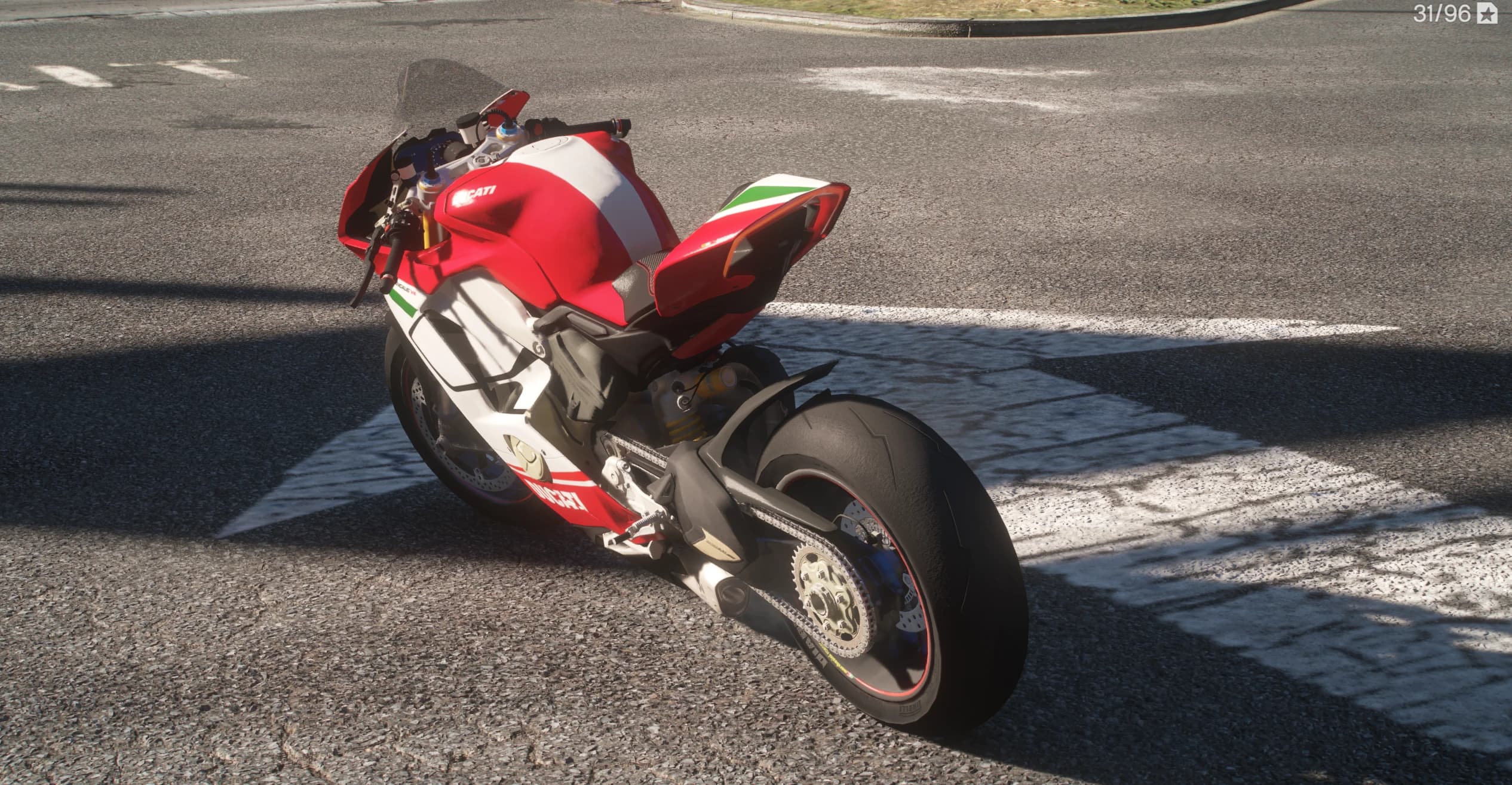 High rear three quarter view over the tricolore tail unit, with the exposed chain, the sprocket and the wide rear tyre on a sunlit crosswalk