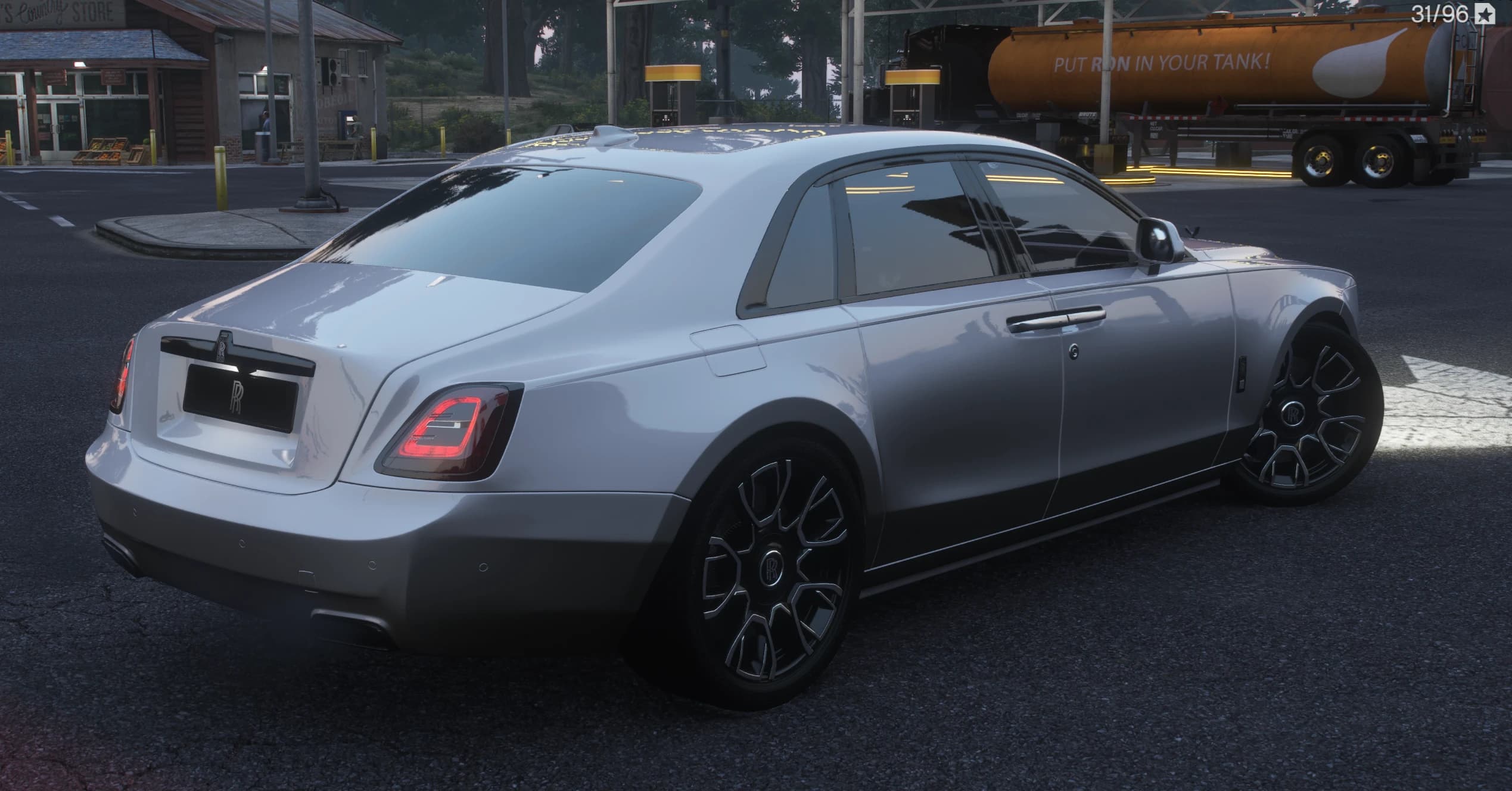 Rear three quarter view at a gas station with the RR monogram on the boot lid, red LED taillights and a fuel tanker truck in the background