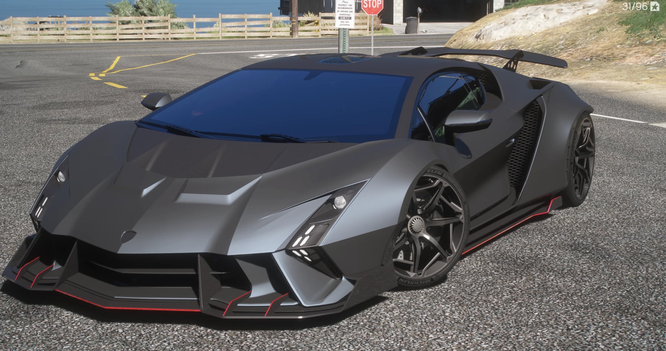 Front three quarter view of the matte grey Lamborghini Invencible with red pinstriped splitter, carbon canards, roof scoop and rear wing on a coastal road