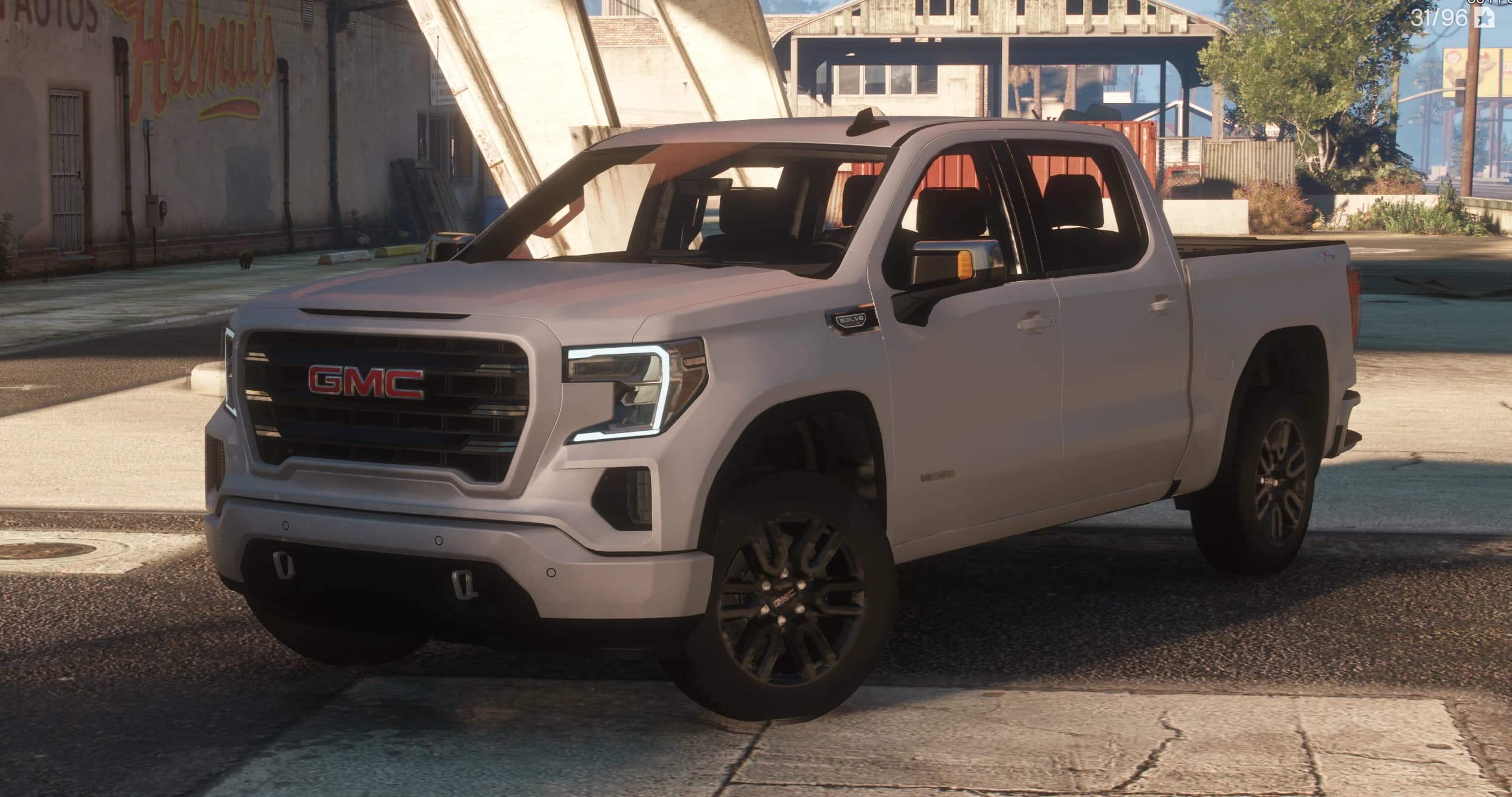 Front three quarter view of the white GMC Sierra AT4 crew cab with the red GMC badge, C shaped daytime lights and the 6.2 V8 emblem on the hood