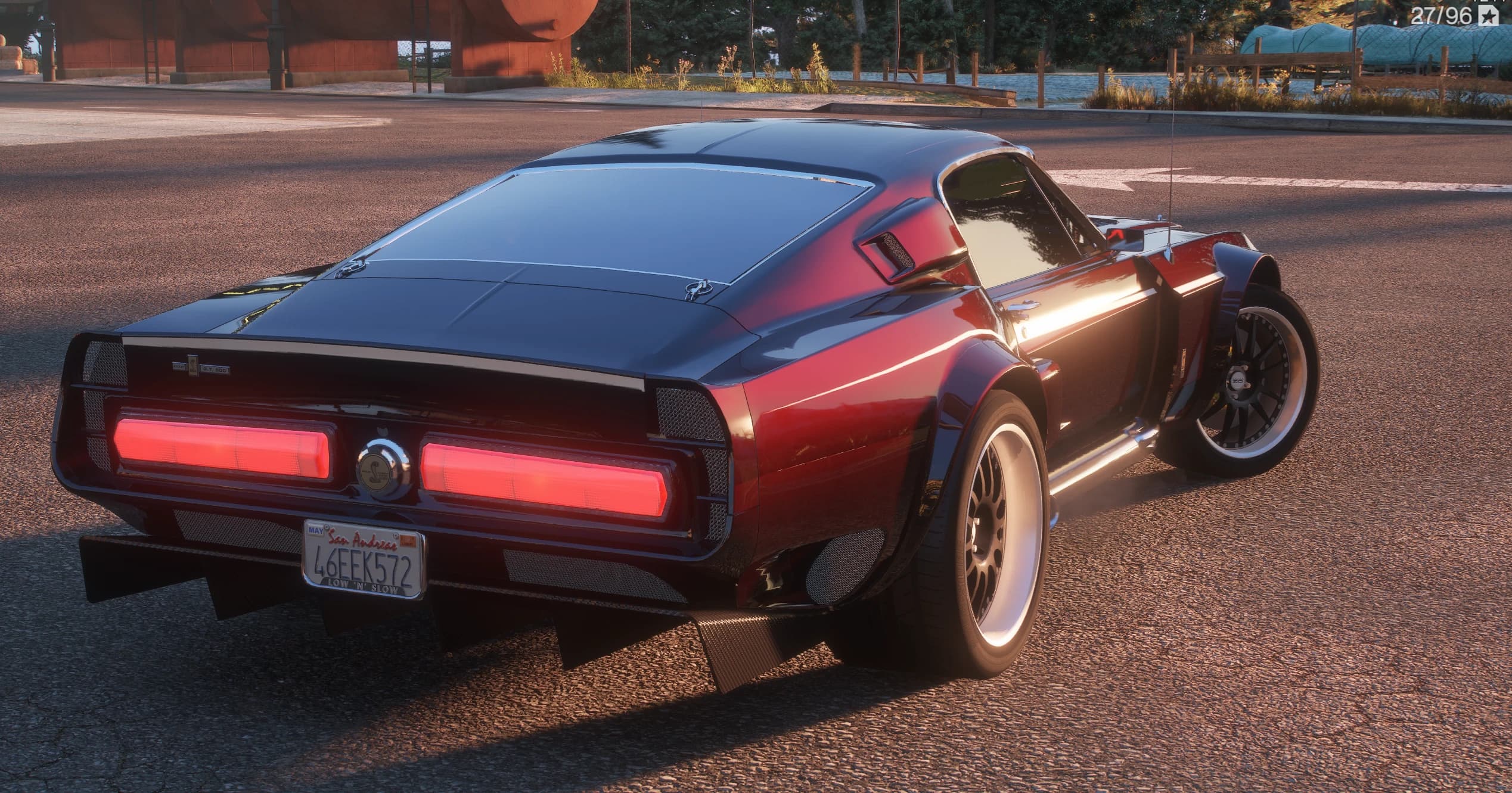 Rear three-quarter of the Shelby showing the candy red rear quarters, two full-width red tail bars with the Shelby snake badge between them, a finned rear diffuser and white-lipped wheels under wide arches