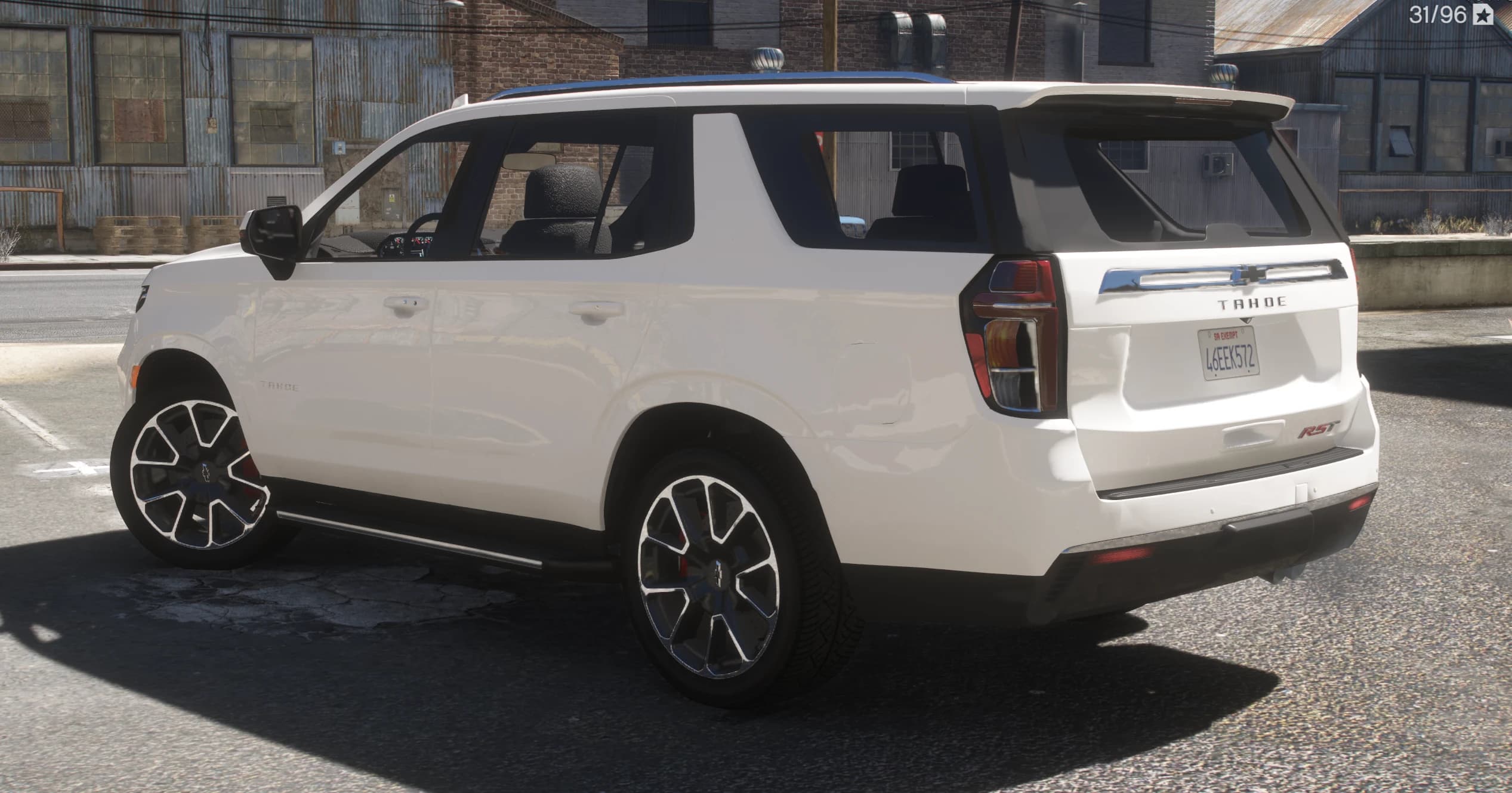 Rear three quarter view by old brick warehouses showing the Tahoe lettering on the tailgate, the RST badge and the chrome bar over the plate
