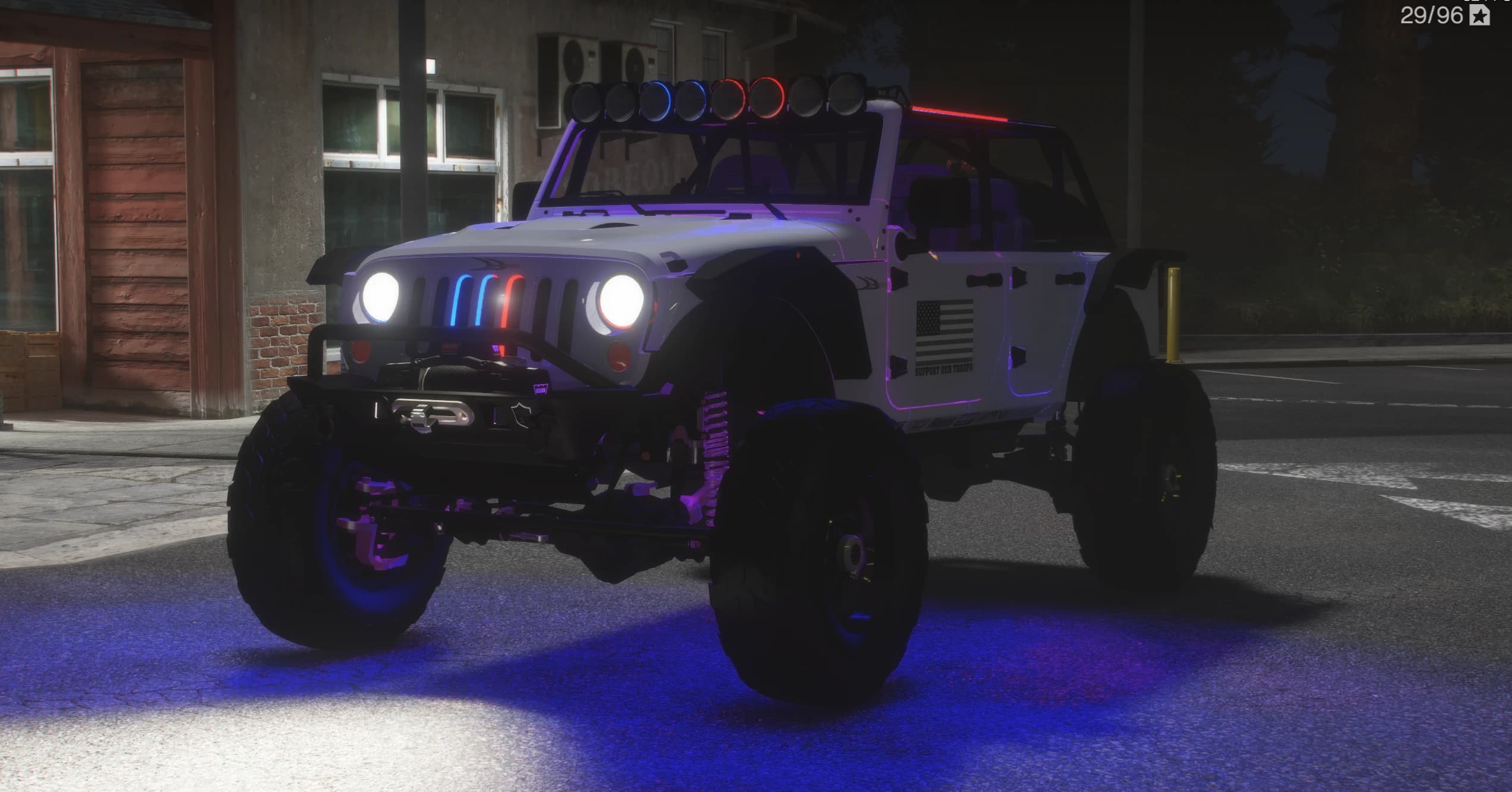 White lifted Jeep Wrangler off-road build at night, with a roof light bar, roll cage, winch bumper, oversized mud tyres and blue underglow, wearing a US flag and Support Our Troops door decals
