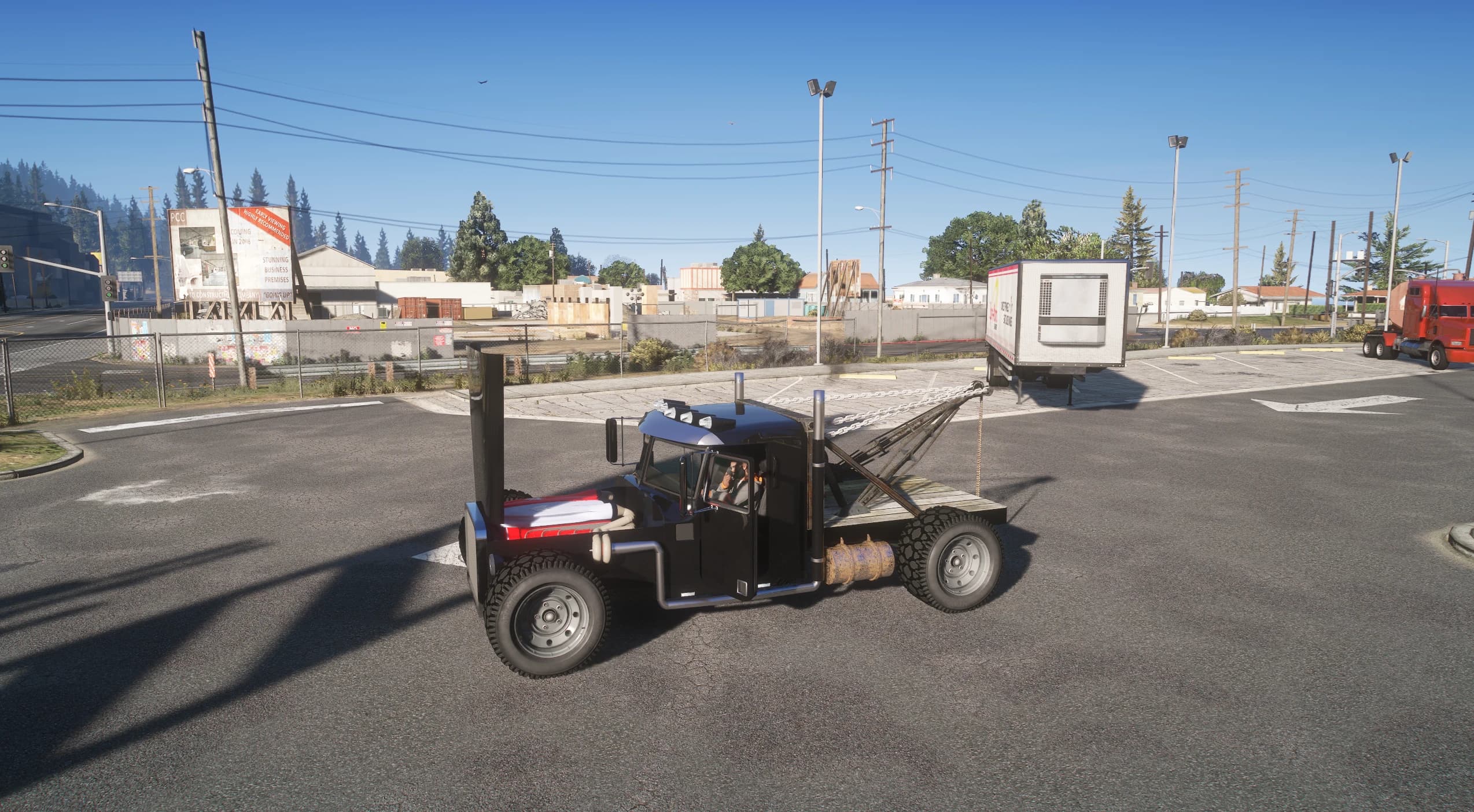 Side view of the Tow-Rod in a parking lot with a driver at the wheel and the tow chain hooked to a white box trailer, an industrial estate and a red truck behind