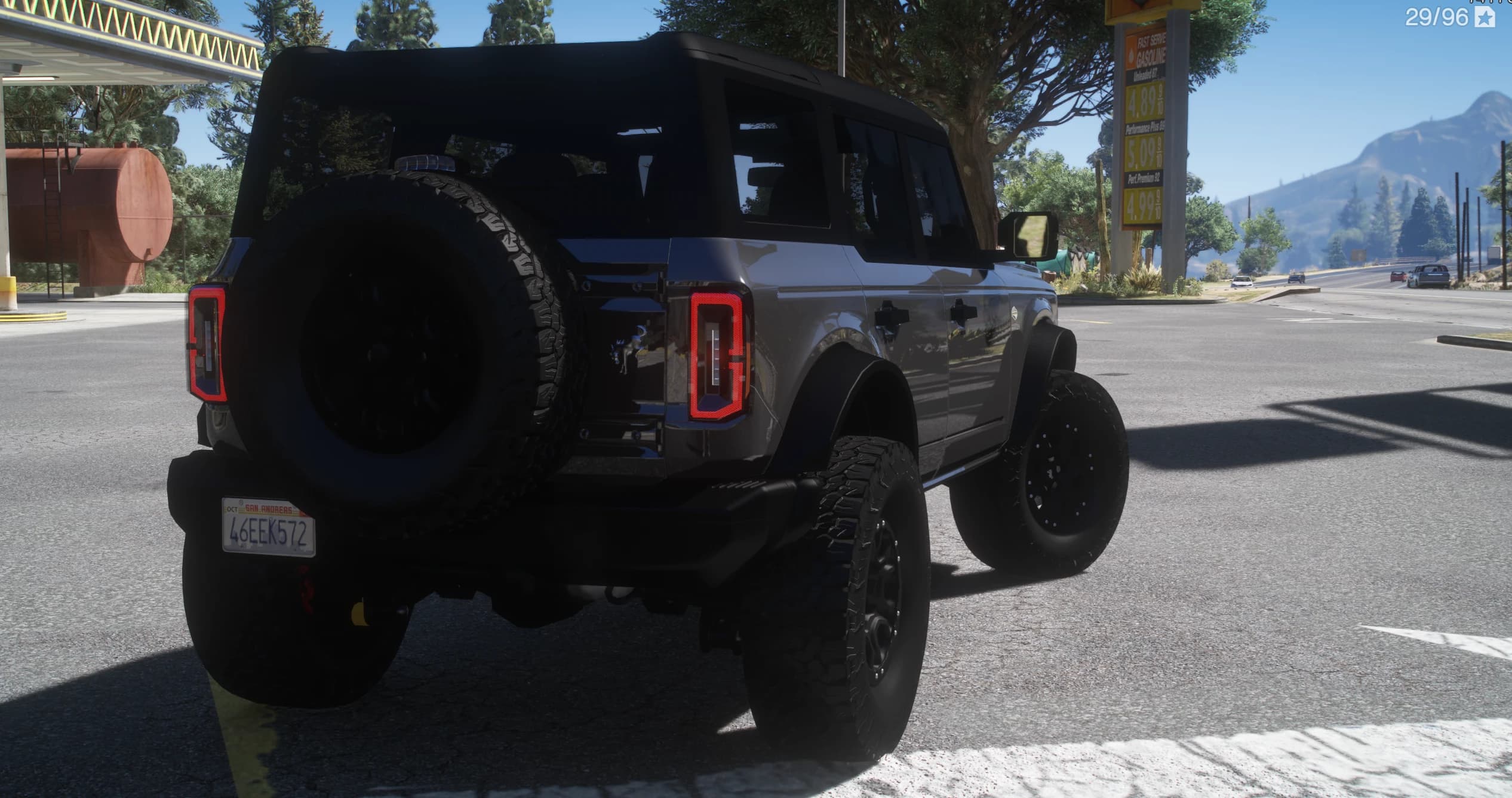 Rear three-quarter of the grey Bronco showing the tailgate-mounted spare wheel and the BRONCO taillights at a gas station