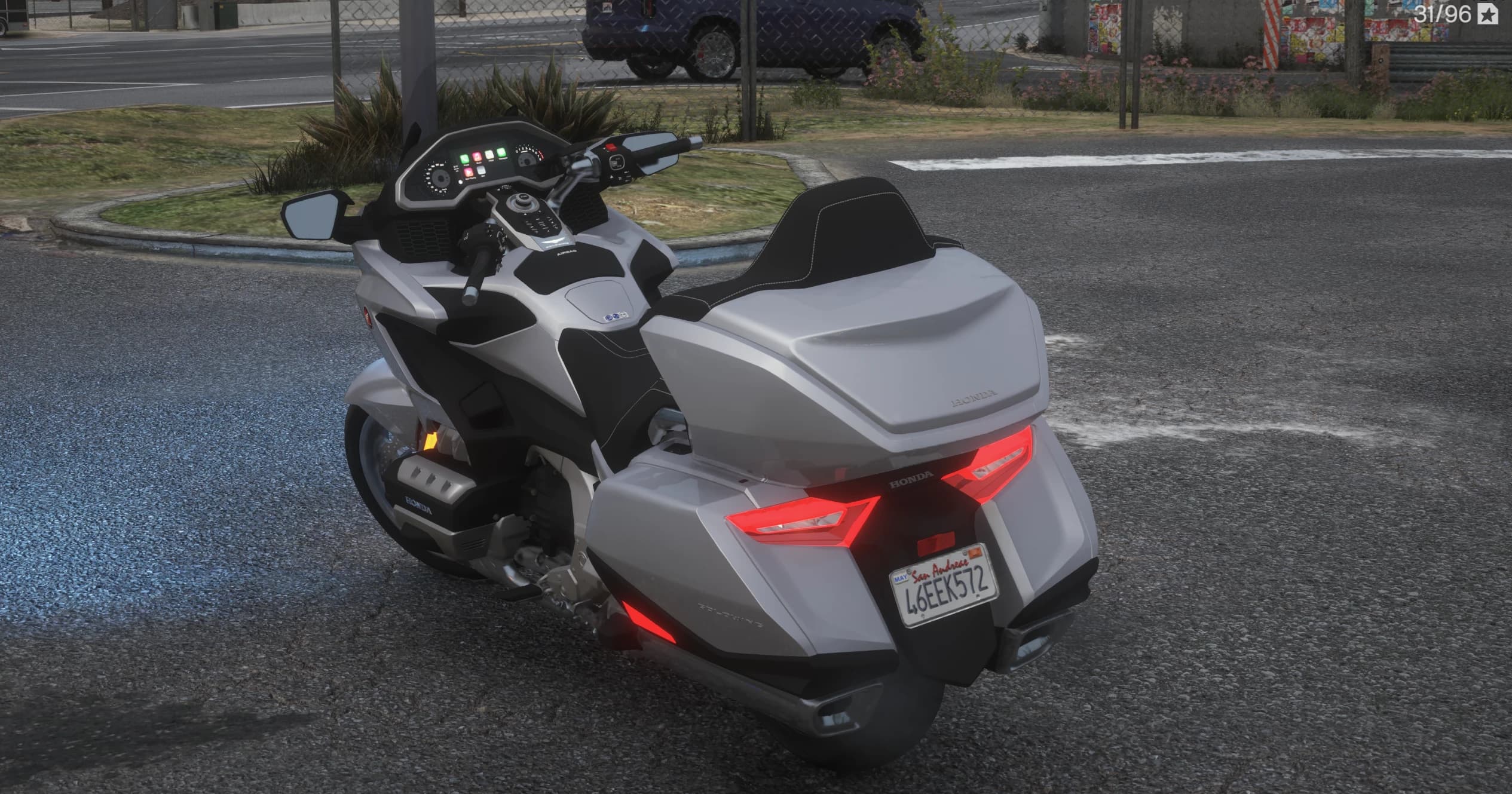 Rear three quarter view showing the lit red taillight bars on the top box and panniers, the San Andreas plate and the rider dash with its screen and switchgear