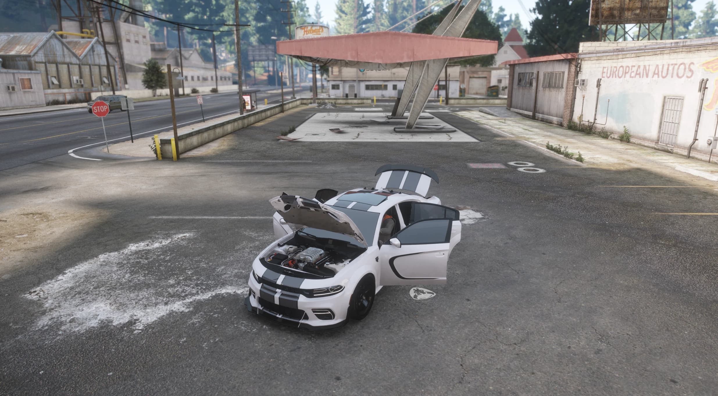 The white Charger at an abandoned gas station with the bonnet and doors open, showing the supercharger on top of the V8