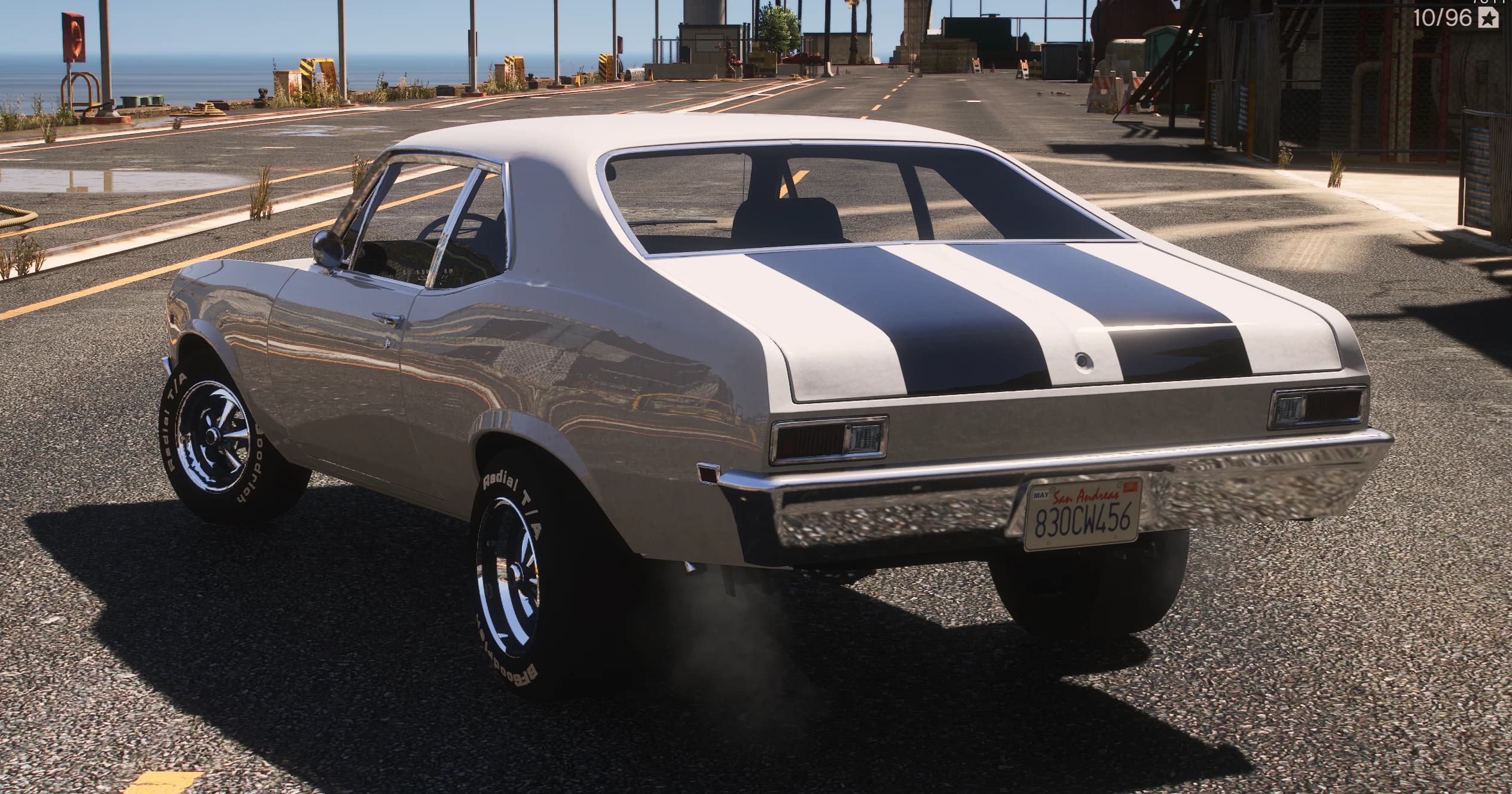 Rear three-quarter of the white Nova with its navy stripes running over the roof and trunk, chrome rear bumper and San Andreas plate 830CW456, on a dockside road by the sea