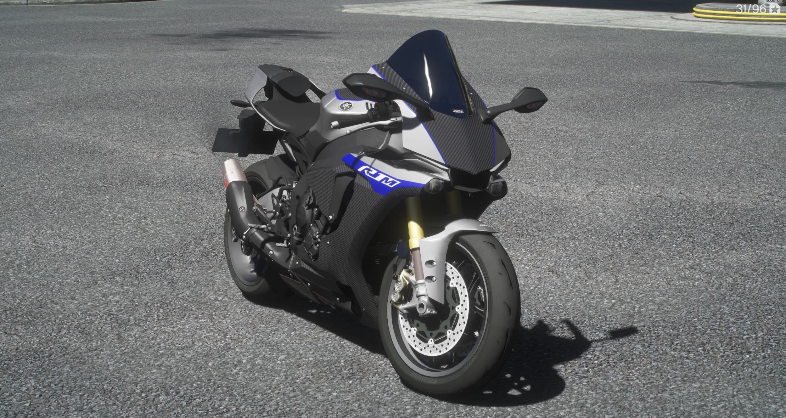 Front three quarter view of the silver and carbon R1M with blue accents, dark blue windscreen, gold forks and carbon lower fairing on a sunlit street