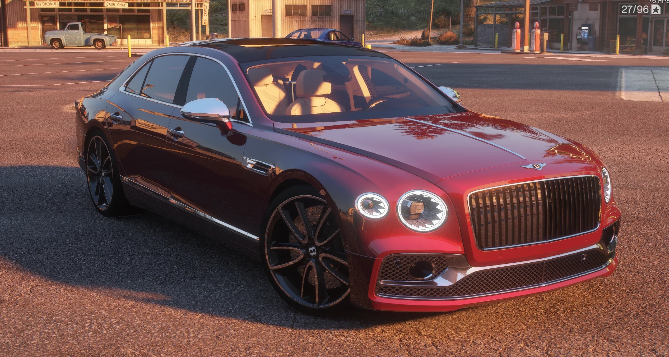 2024 Bentley Flying Spur W12 in cherry red with a black roof, front three-quarter in low sunlight, chrome mesh grille with the winged B, round cut-crystal headlights and black multi-spoke wheels