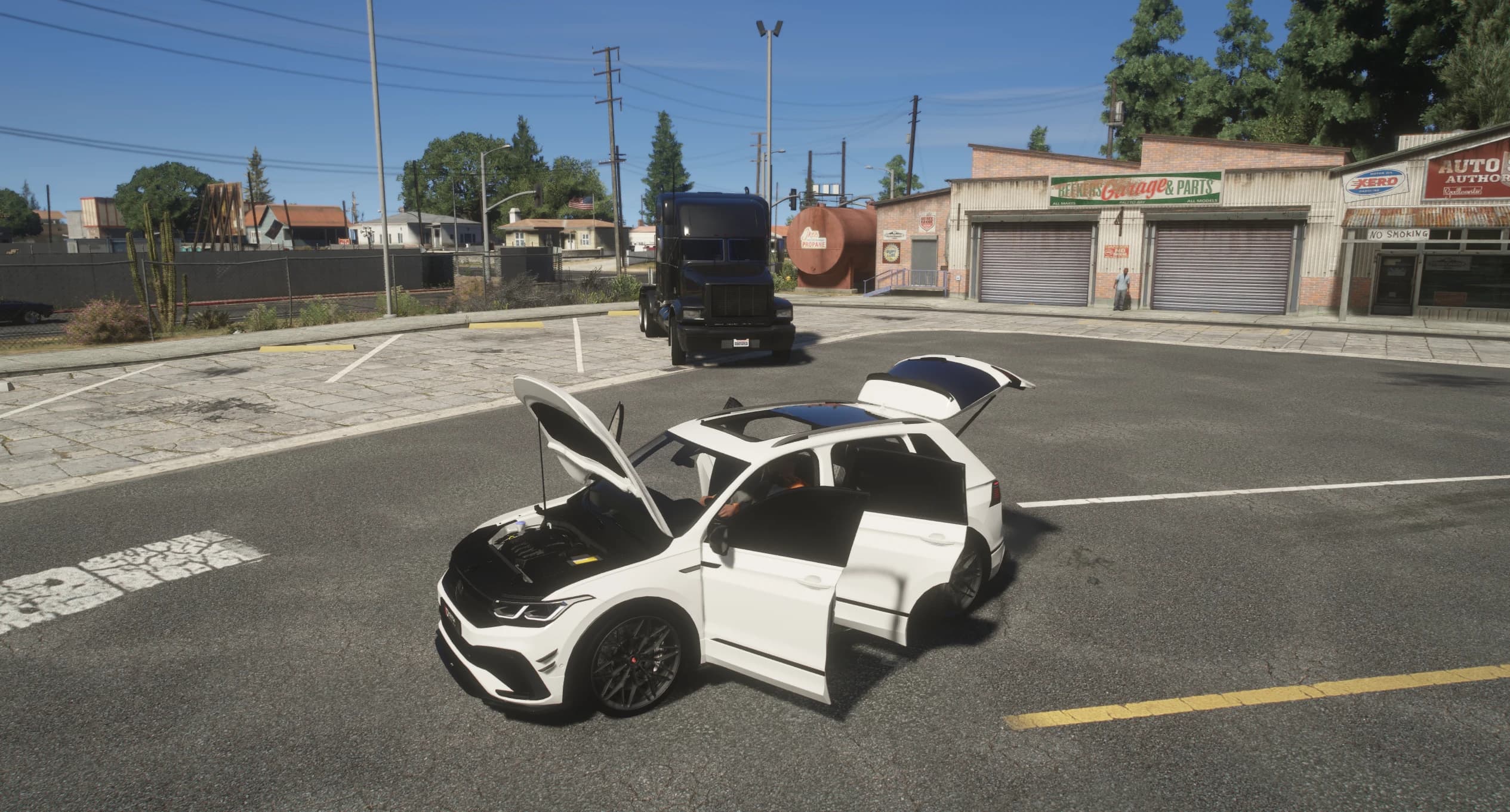 The Tiguan in a parking lot with the hood, the doors and the tailgate open, showing the engine bay and the panoramic glass roof, with a garage and a black semi behind