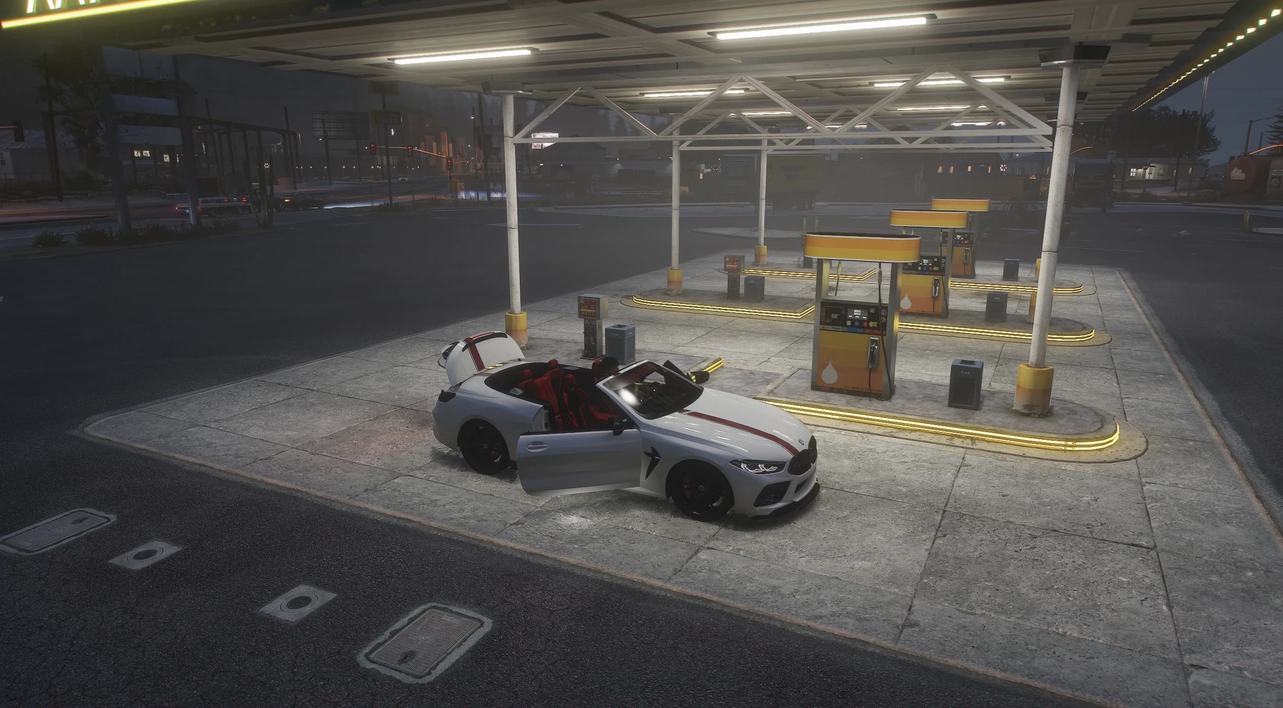 High angle of the MH8 800 on a lit petrol station forecourt at dusk, with the driver's door open and the roof compartment cover raised over the stowed folding top