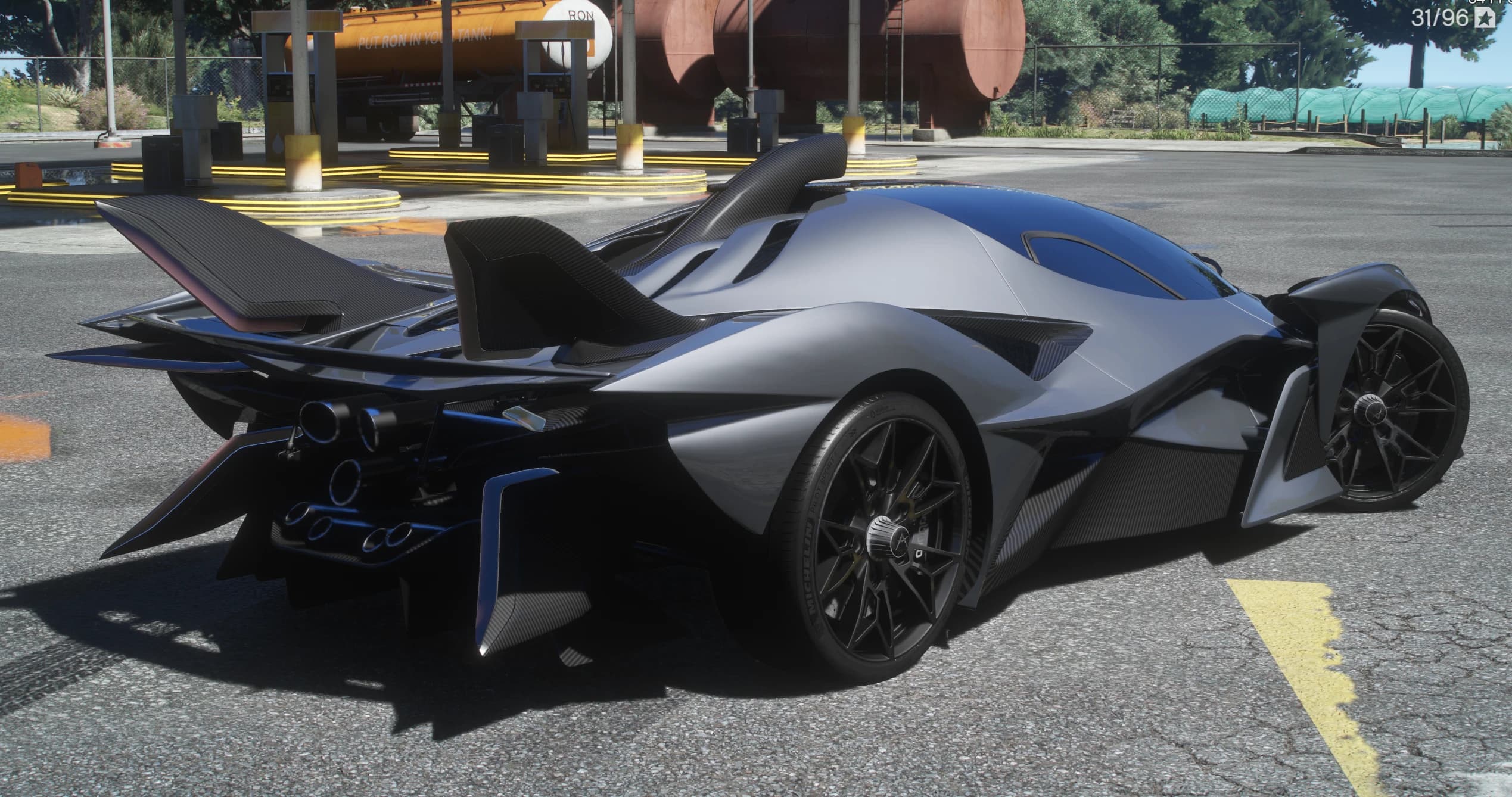 Rear three quarter view at a rural gas station with the carbon rear wing raised, the roof air scoop and the round exhausts stacked in the tail