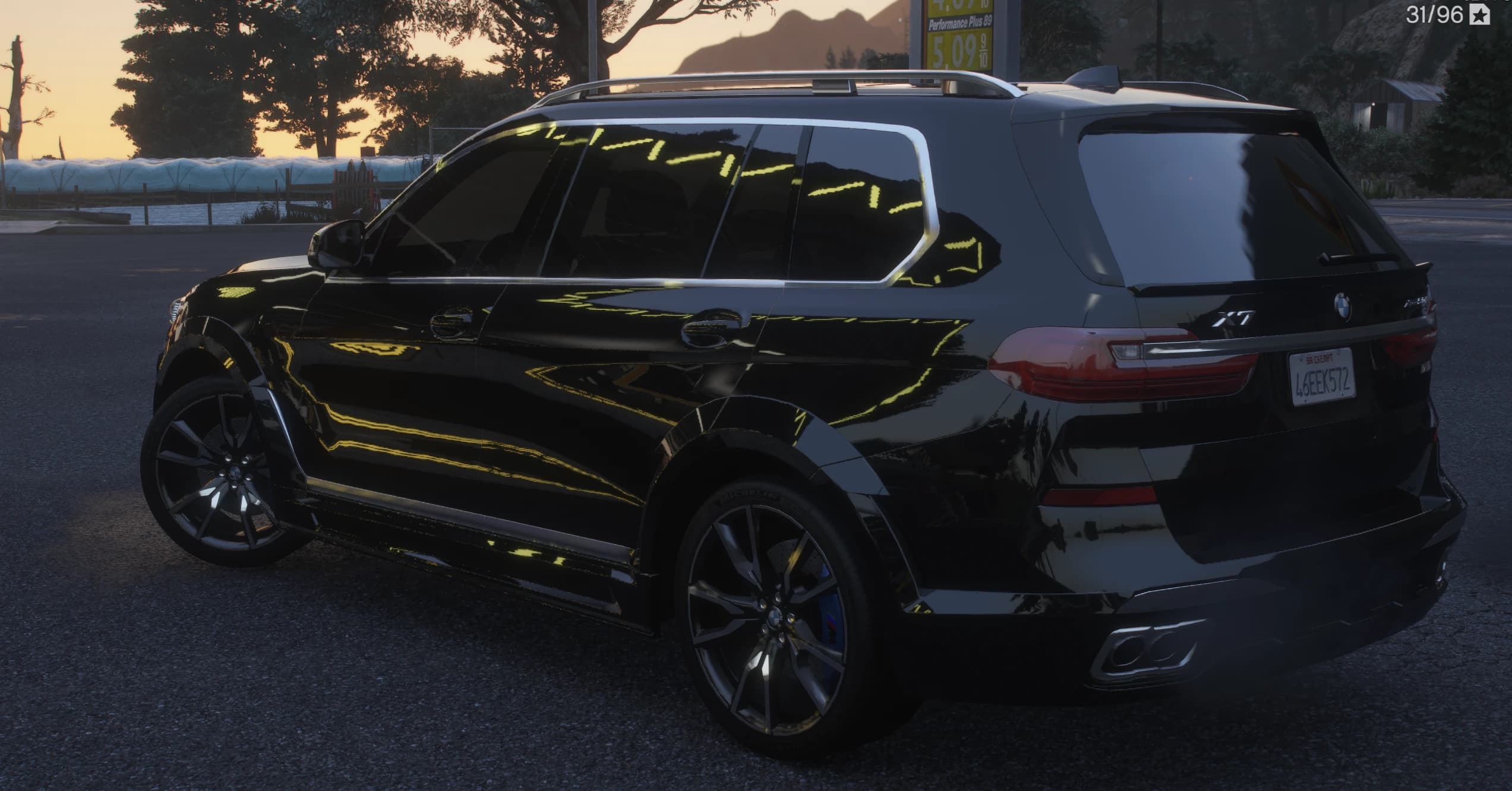 Rear three quarter view at sunset with the X7 badge, slim taillights, roof rails and rectangular exhaust tips next to a gas station price sign