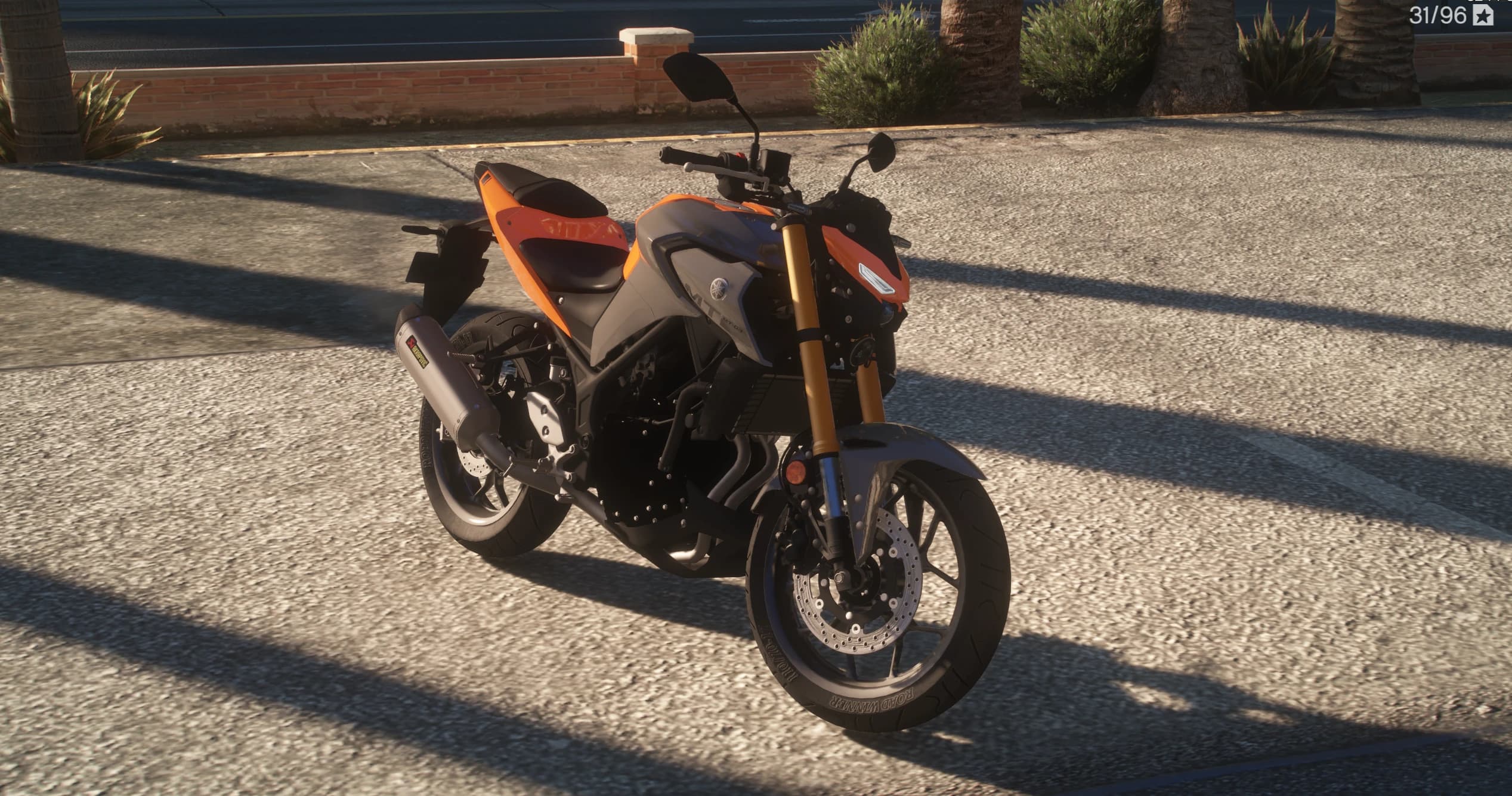 Front three quarter view of the orange and grey Yamaha MT-03 with gold upside down forks, twin front discs and an Akrapovic silencer, parked by a brick wall