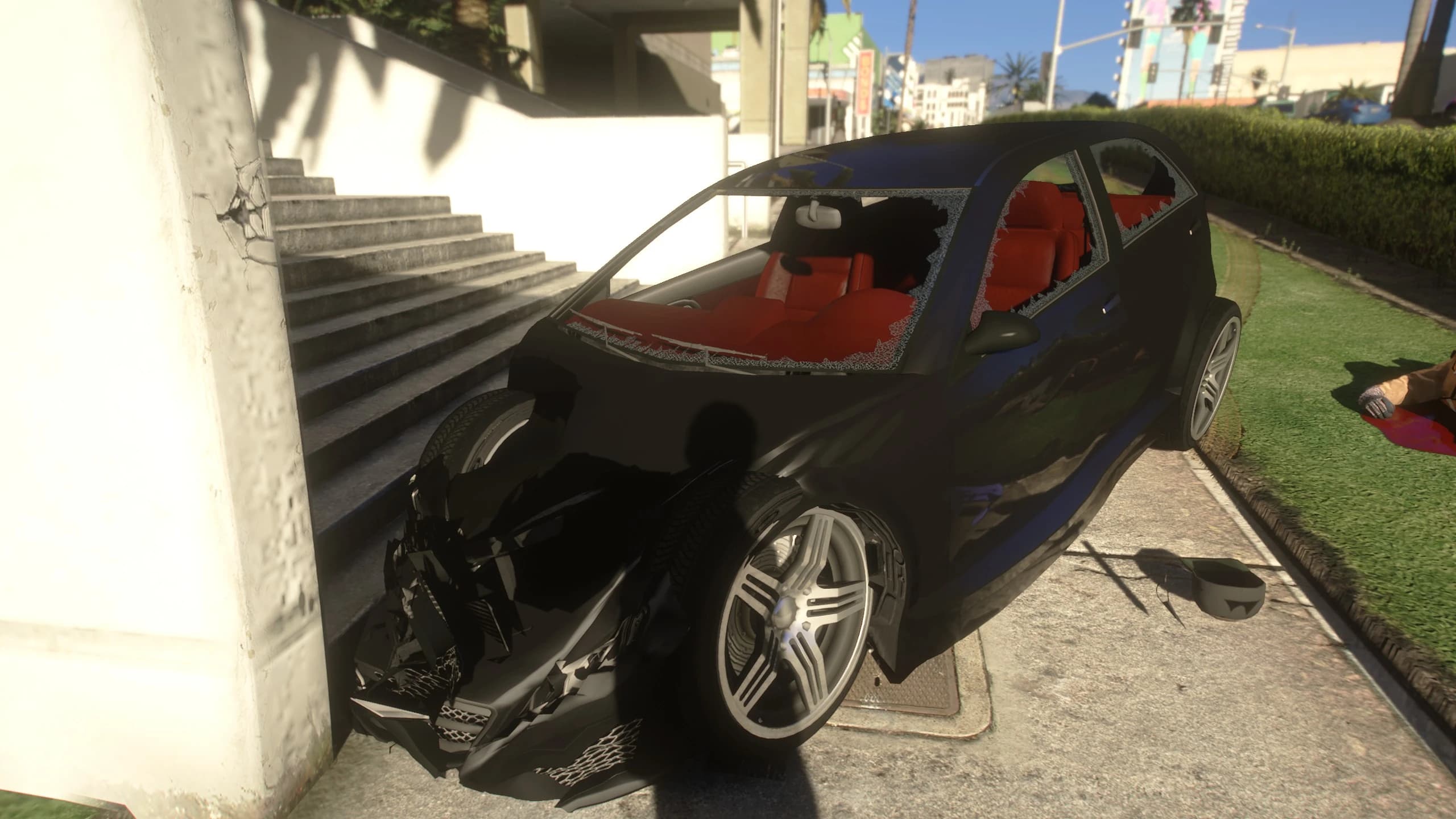 Black hatchback folded against a concrete staircase: the whole front end is crumpled, the wheel is torn out and the red interior shows through the broken glass