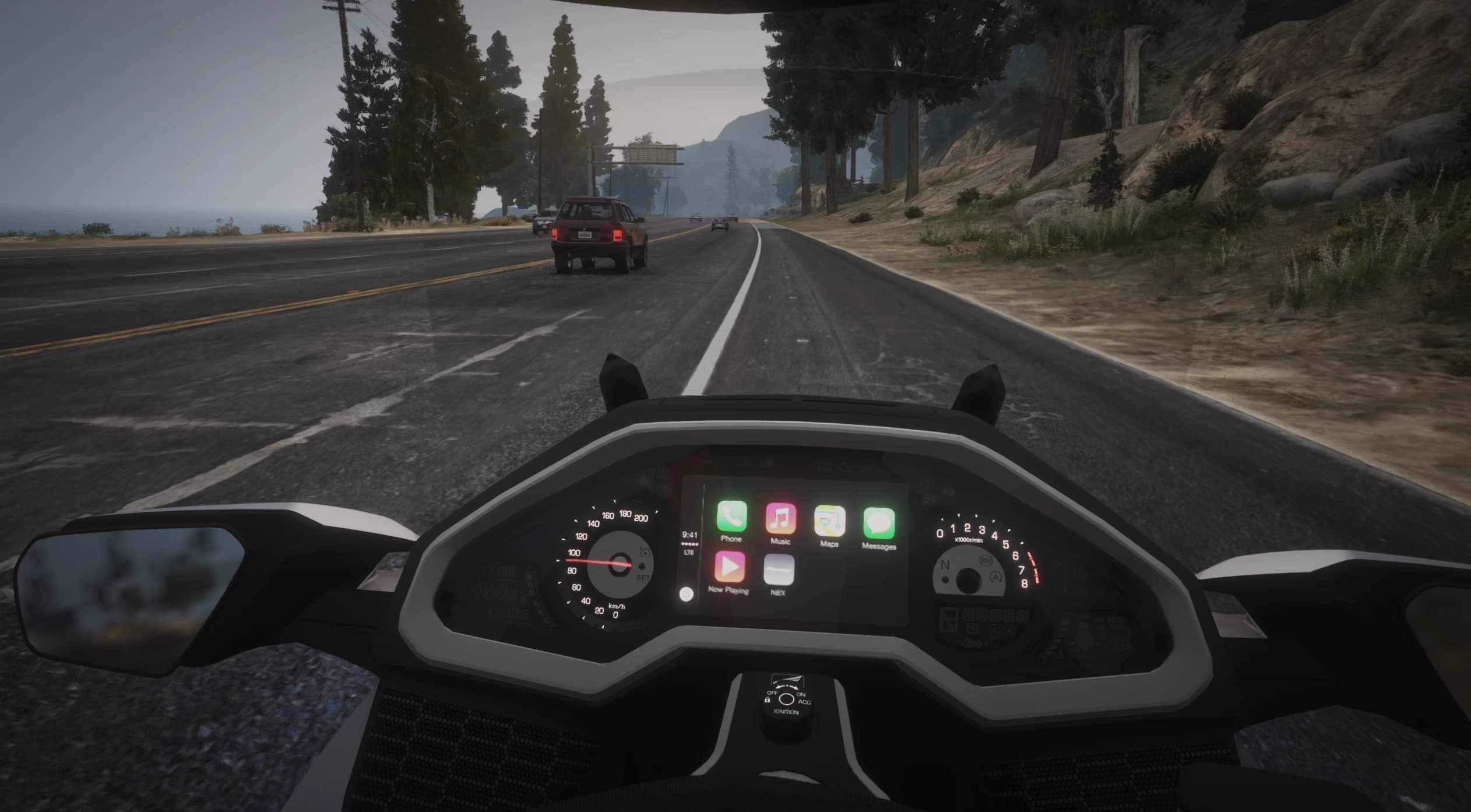 First person riding view on a coastal highway with the full Goldwing dash, analog speedo and tach and the centre touchscreen showing phone, music and map apps