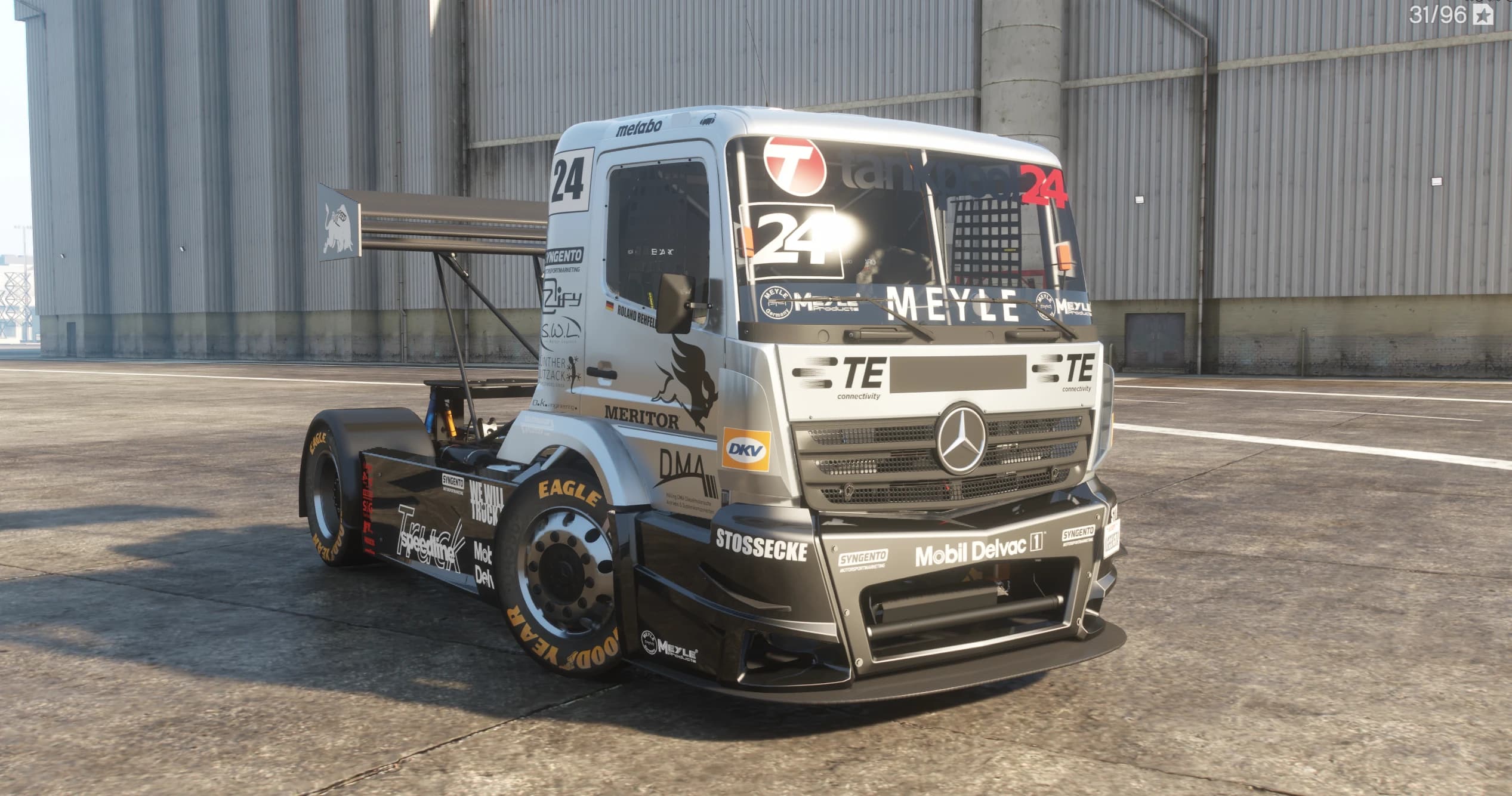 Front three quarter view of the silver and black number 24 Mercedes race truck with the MEYLE windscreen banner, sponsor decals and the tall rear wing, parked by industrial silos