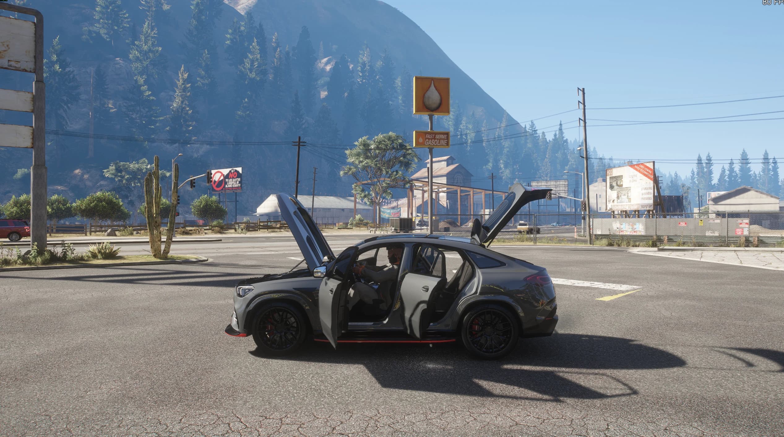 Side view of the GLE at a Route 68 junction with both left doors and the tailgate open at once and the driver sitting at the wheel, mountains and a petrol station sign behind