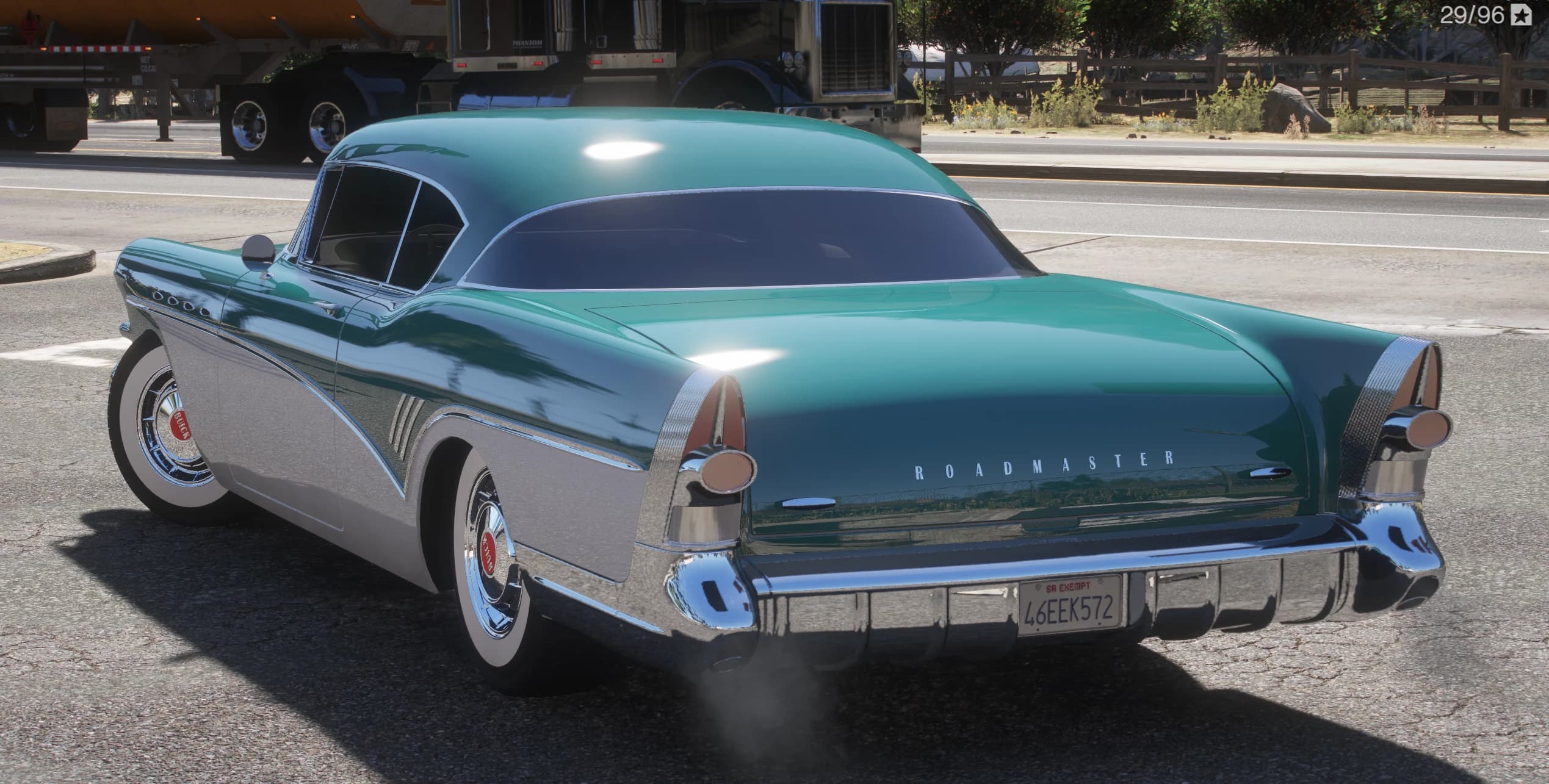 Rear three-quarter of the two-tone Buick Roadmaster showing the ROADMASTER script on the fender, chrome tailfins and bumper on a country highway