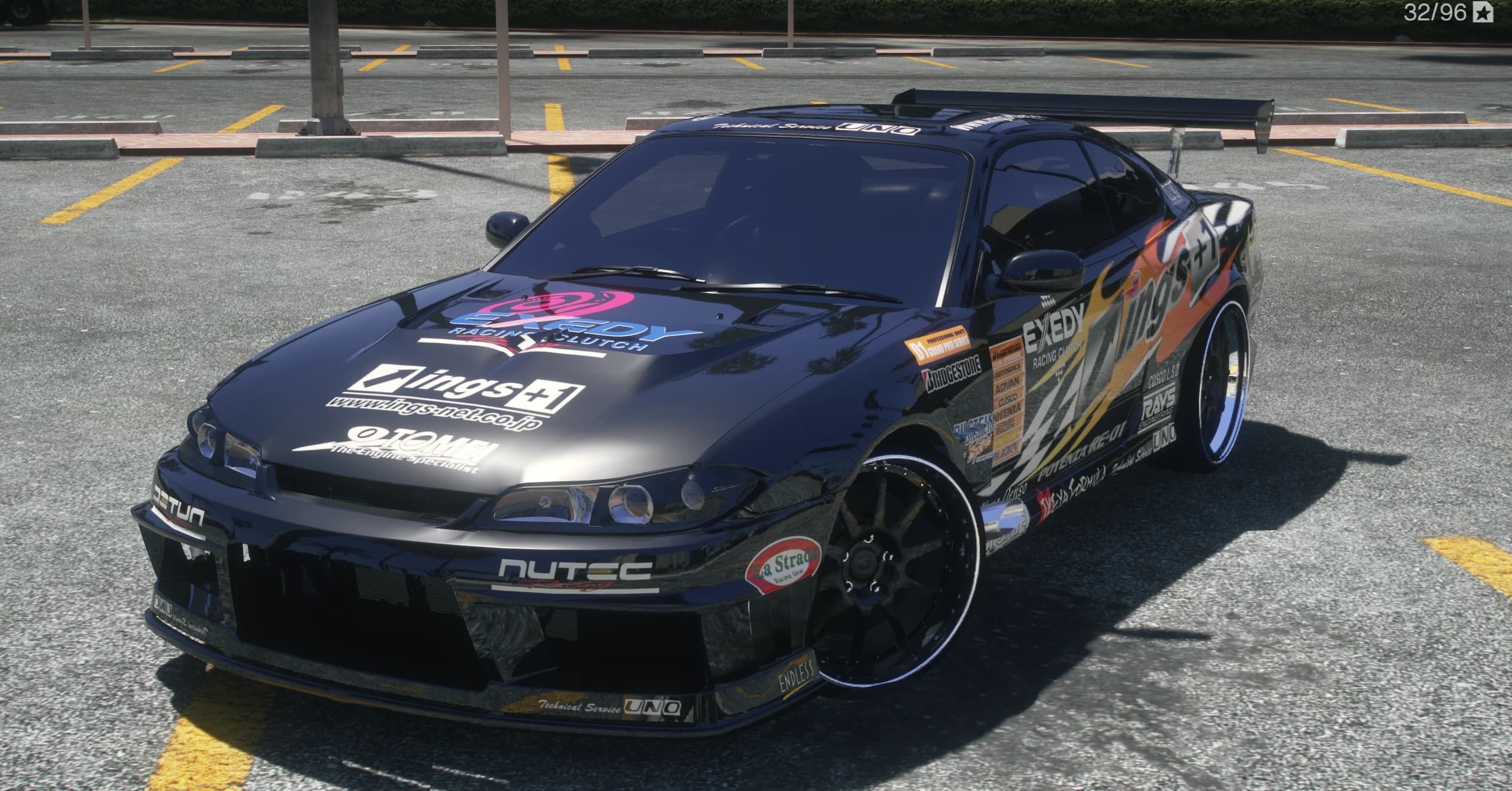 Front three quarter view of the black Silvia S15 in the ings+1 flame livery with EXEDY hood logo, sponsor stack on the door and a tall GT wing