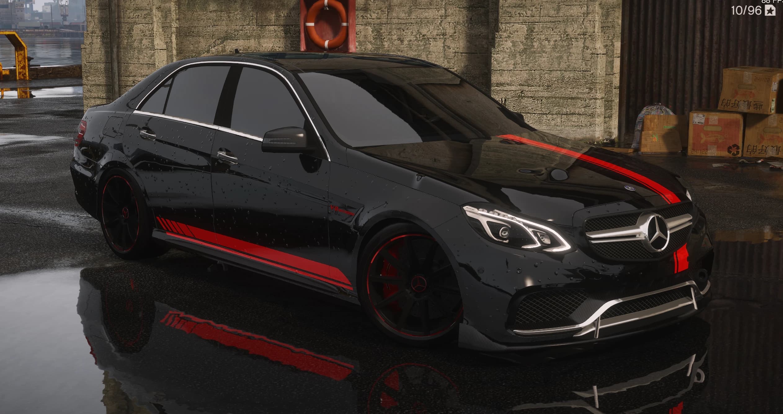 Black Mercedes-Benz E63 S AMG sedan with a red racing stripe and red-lipped black wheels, front three-quarter view on a wet dock