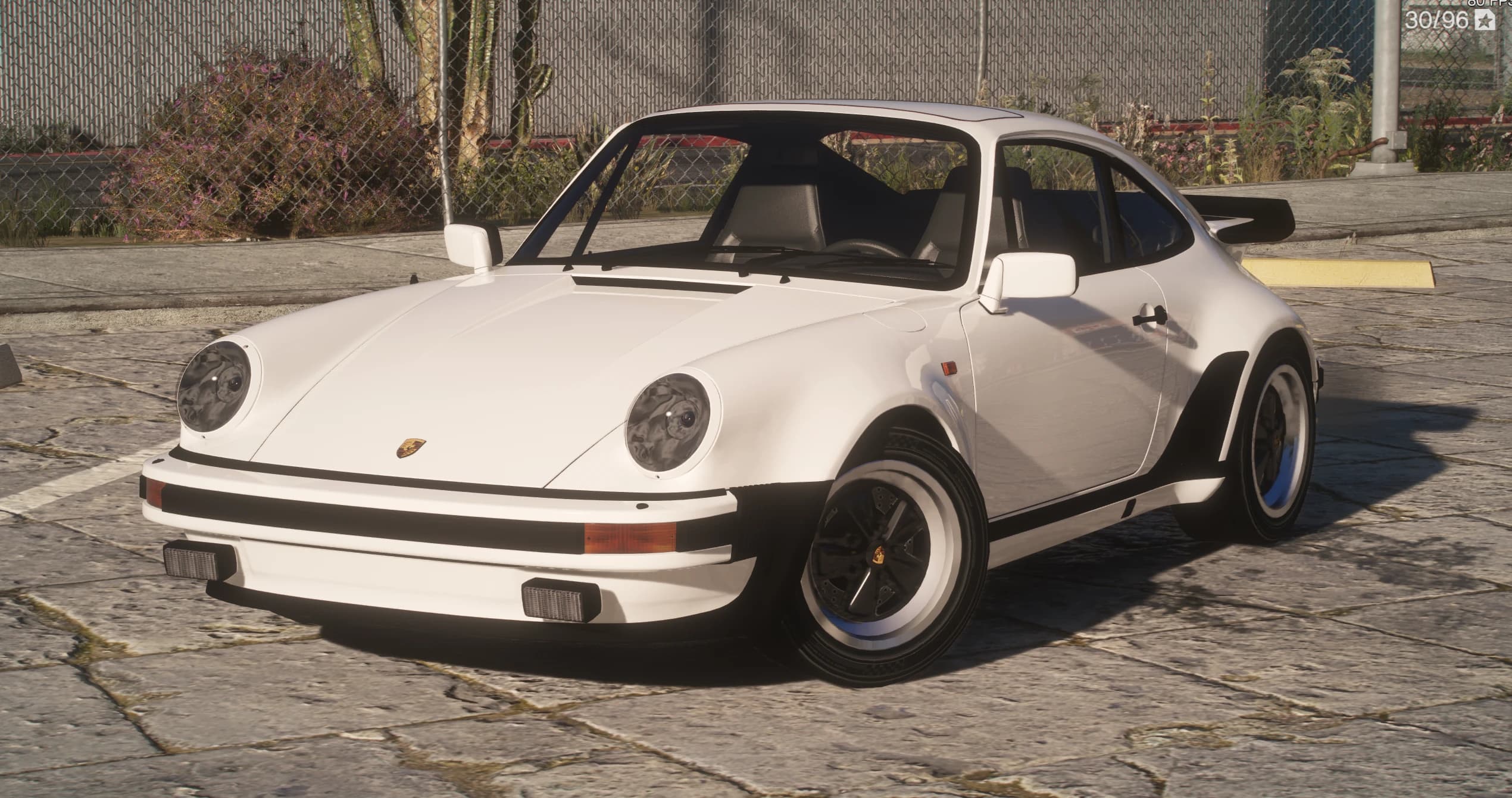 White 1982 Porsche 911 Turbo 3.3, front three-quarter view on stone paving, showing the round headlights, black rubber-strip bumpers, the Porsche crest on the hood and staggered Fuchs-style wheels under flared arches
