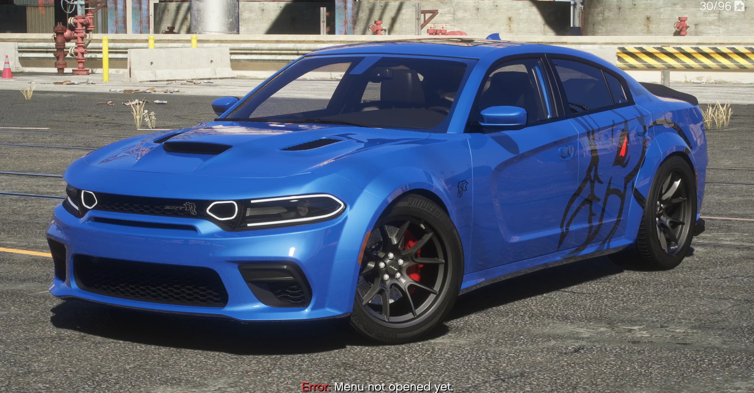 Blue 2024 Dodge Charger Hellephant widebody, front three-quarter view in an industrial refinery yard, showing the SRT grille badge, dual hood scoops, a black tribal graphic on the flank and gunmetal wheels with red brake calipers