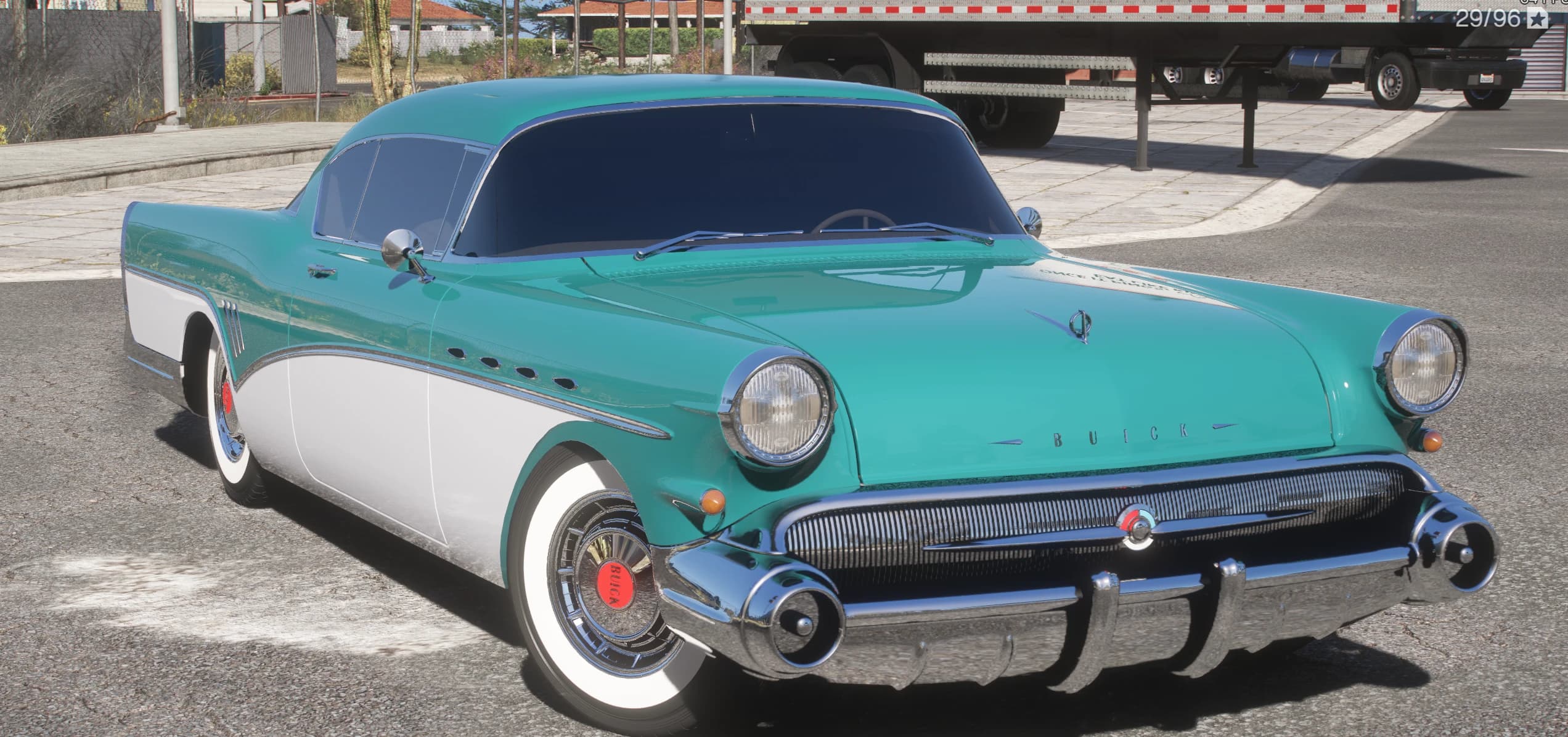 Teal and white 1957 Buick Roadmaster, front three-quarter view with a chrome grille, hooded headlights and wide whitewall tyres, parked at a desert truck stop